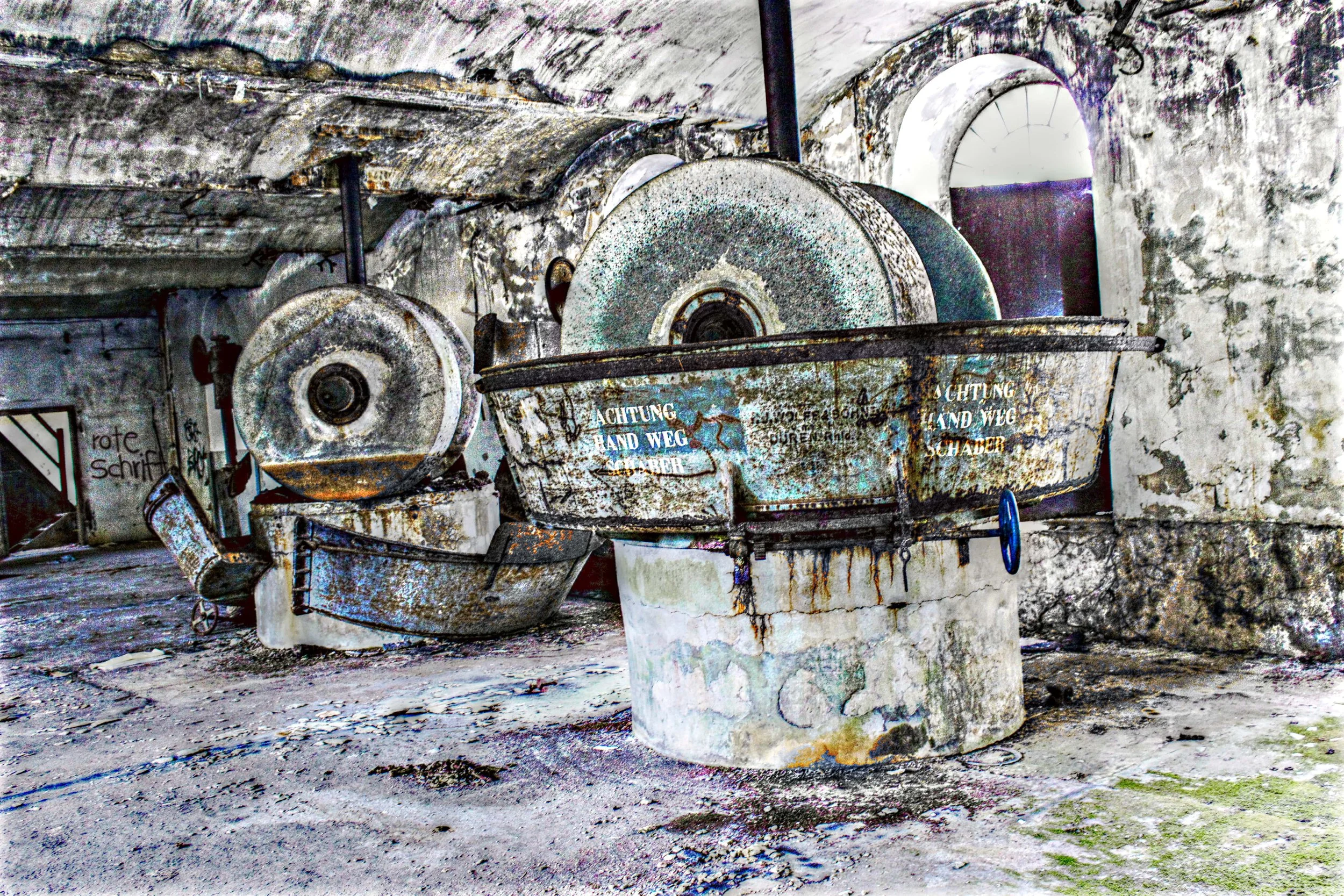 Ein verrosteter, alter Brunnen in einer verfallenen, beschädigten Räume, mit Schmutz und Graffiti an den Wänden.