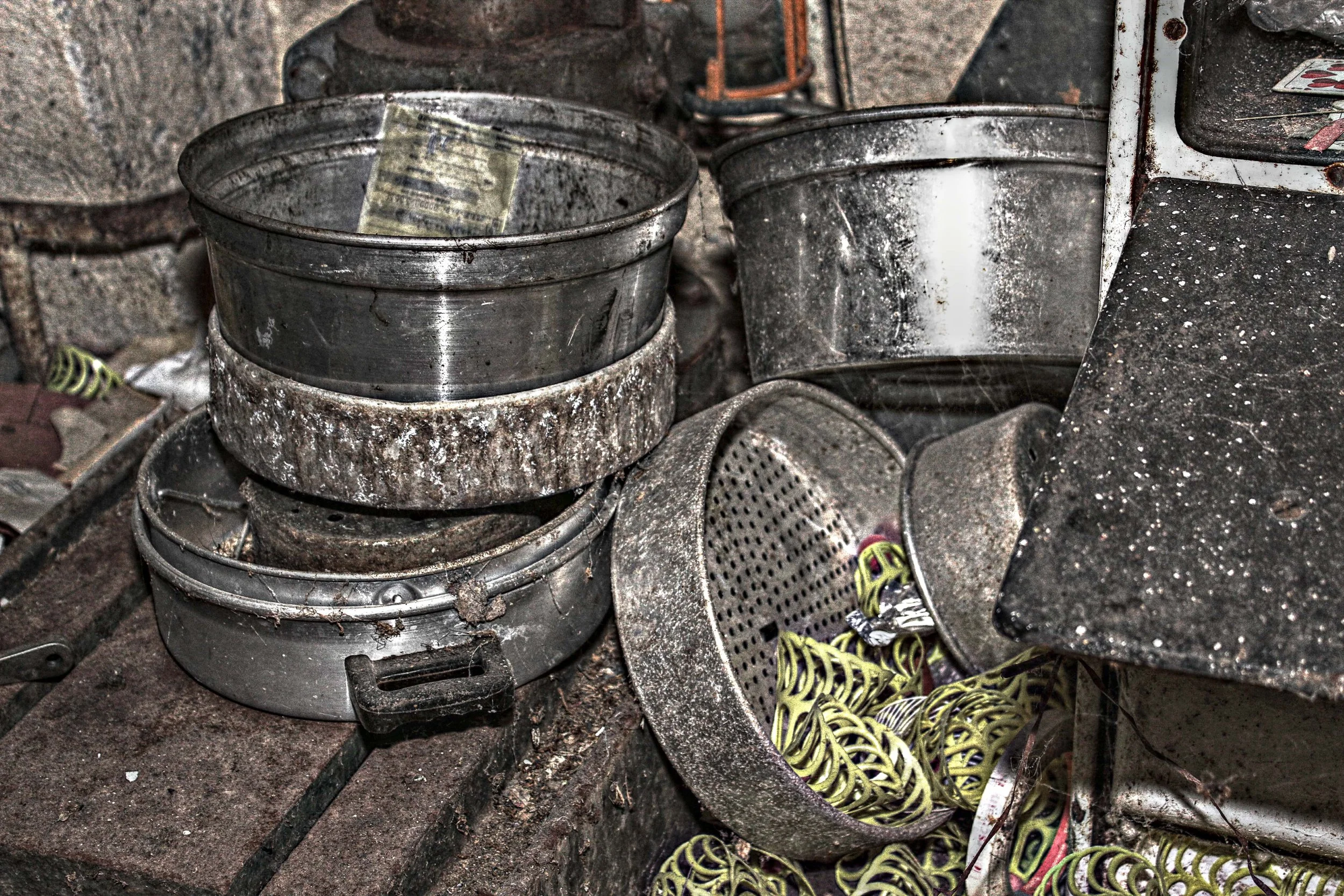 Eine Ansammlung von metallenen Backformen, Sieben und Ringen, die schmutzig und rostig sind, auf einem alten Backtisch in einer staubigen Küche.