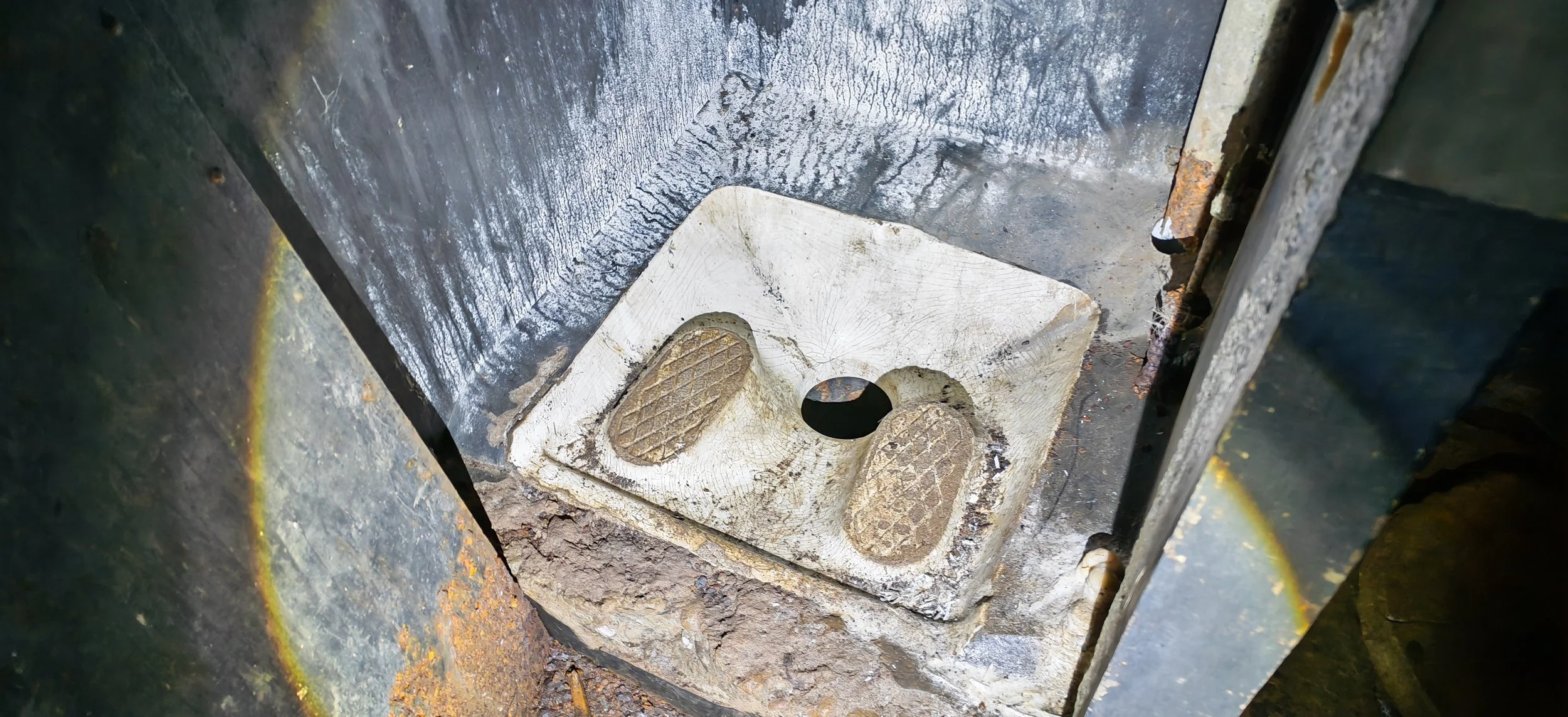 Innenansicht eines alten, verrosteten Metallteils mit einem weißen Kunststoff- oder Gummiteil, das zwei rutschfeste Oberflächen hat und zwei Löcher, vermutlich für Befestigungen oder Führungen.
