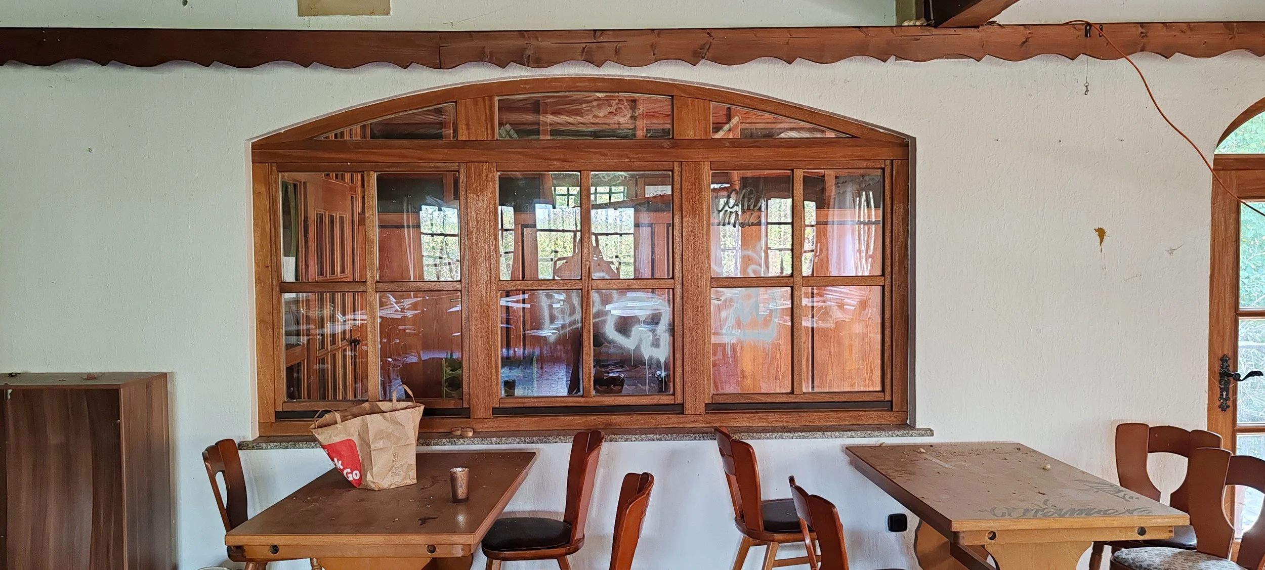 Innenraum mit Holzdekor, Tischen, Stühlen und großen Fenster mit Holzrahmen.