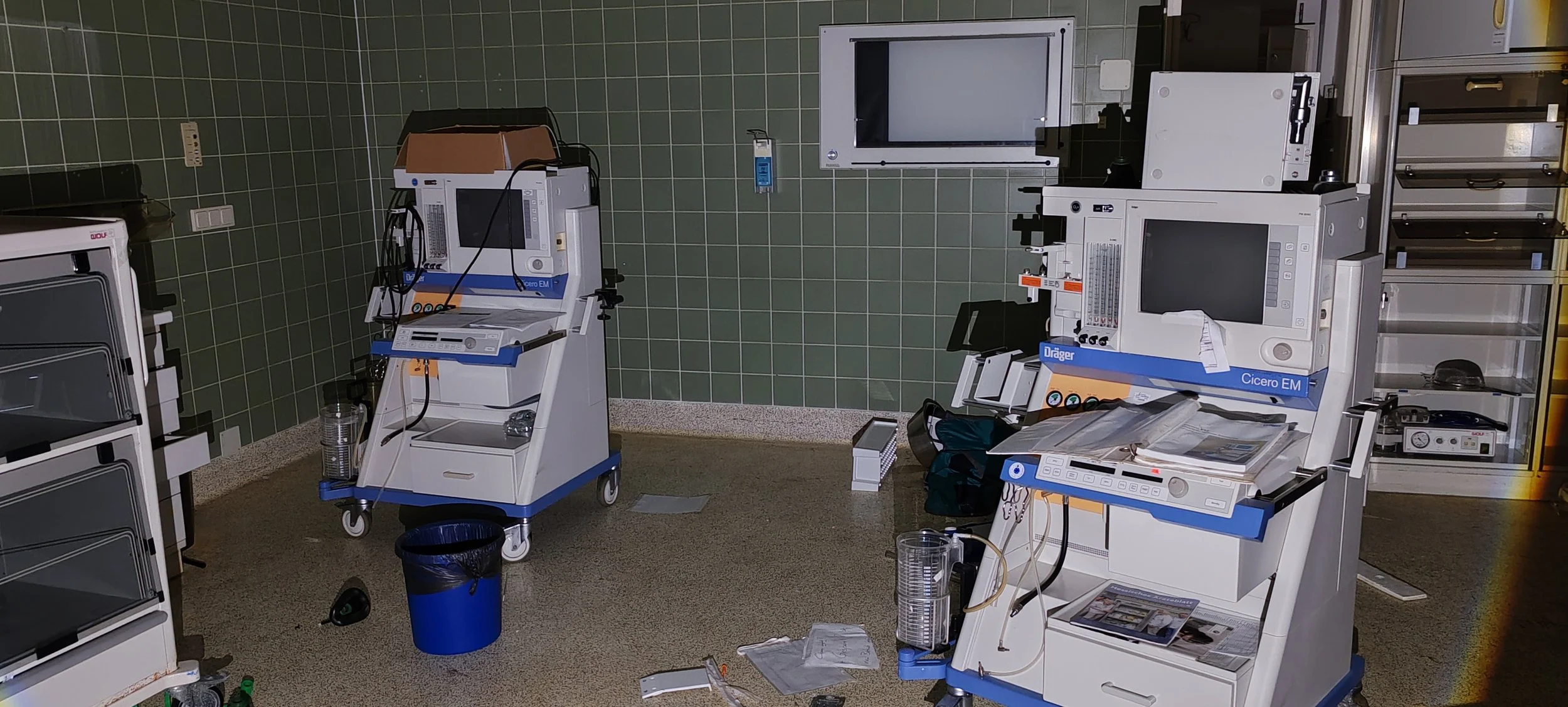 Medizinische Geräte in einem Behandlungsraum, darunter Überwachungsmonitore und medizinische Ausstattung, auf einem sauberen Boden mit einigen verstreuten Gegenständen.