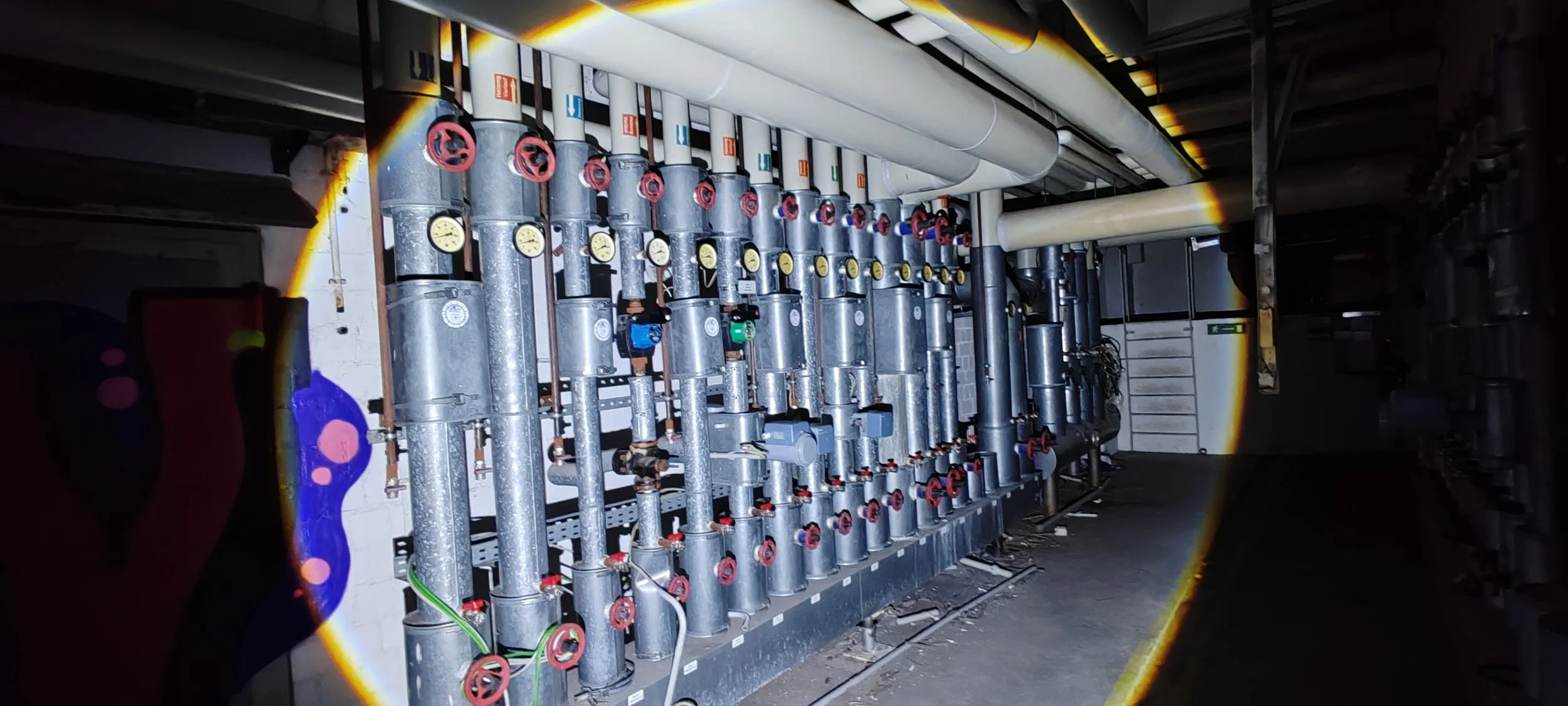 Innenansicht einer technischen Anlage mit mehreren Rohren, Ventilen und Druckanzeigen, vermutlich Teil eines Heizungs- oder Wasserverteilungssystems.