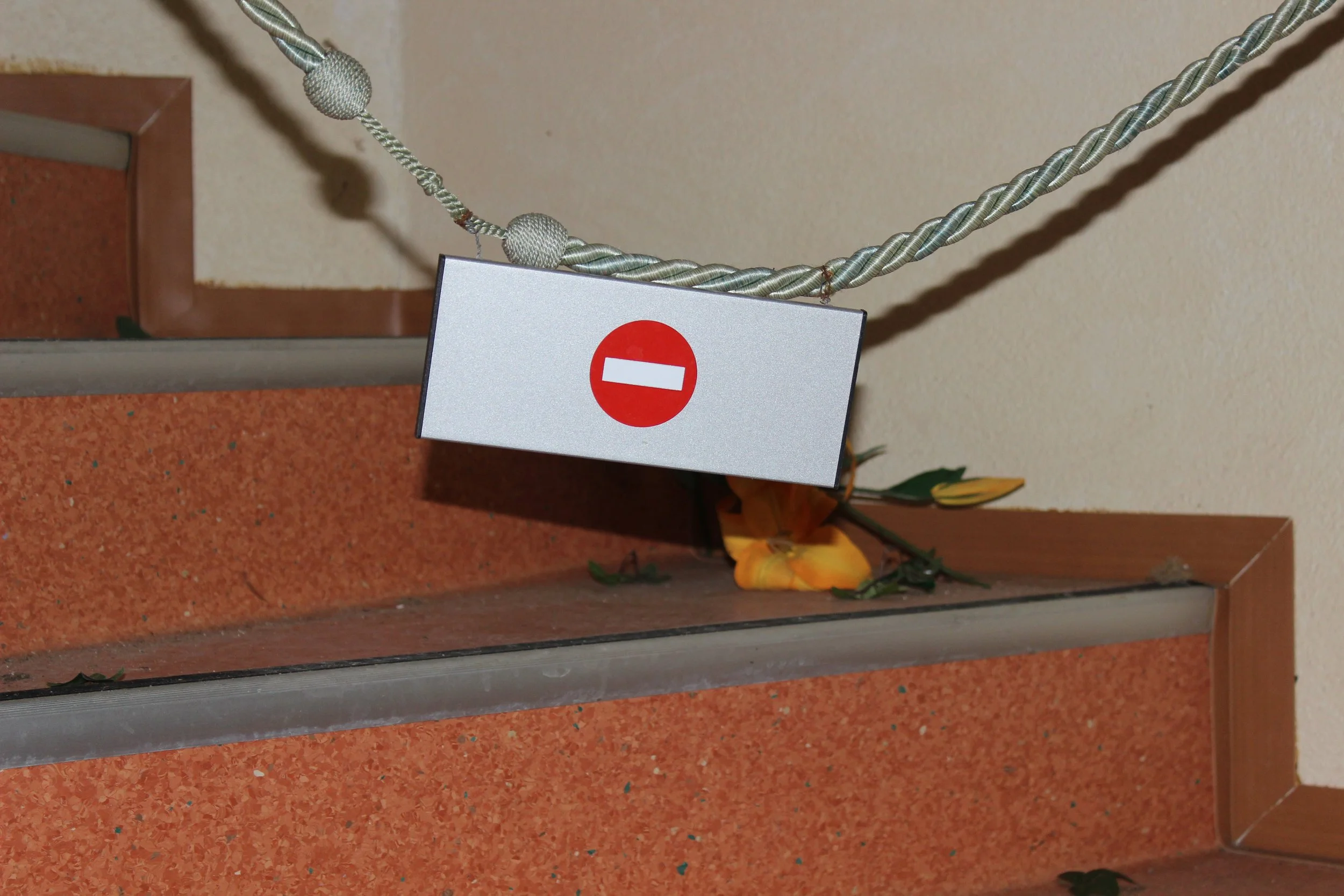 Ein Stopp-Schild hängt an einer Schnur zwischen Treppenstufen und einer Wand. Darunter liegen Blumen auf den Stufen.