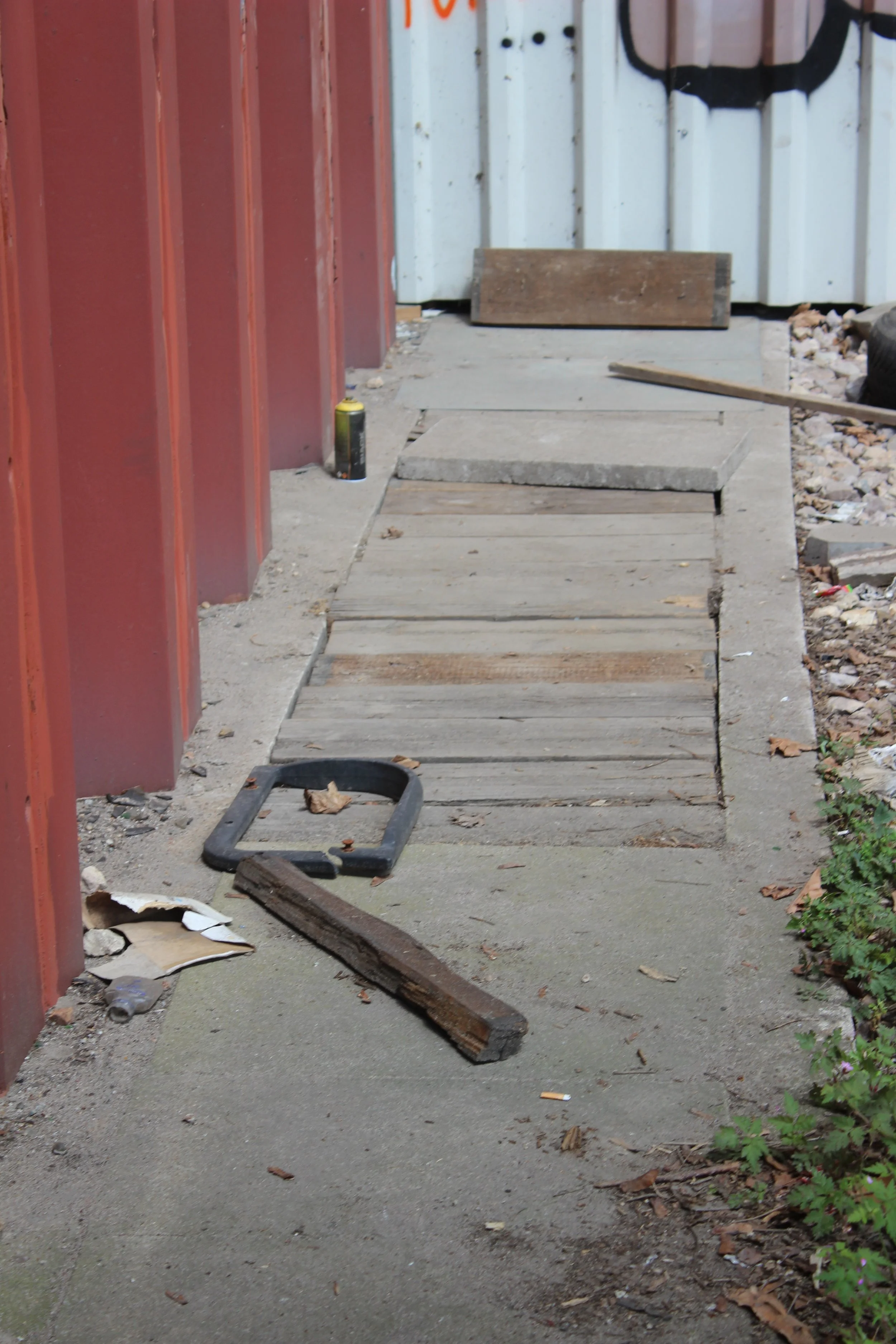 Baustelle mit Pflastersteinen, Holzstücken und Werkzeug an einem Gehweg neben einem Gebäude mit rotem und weißen Wänden.