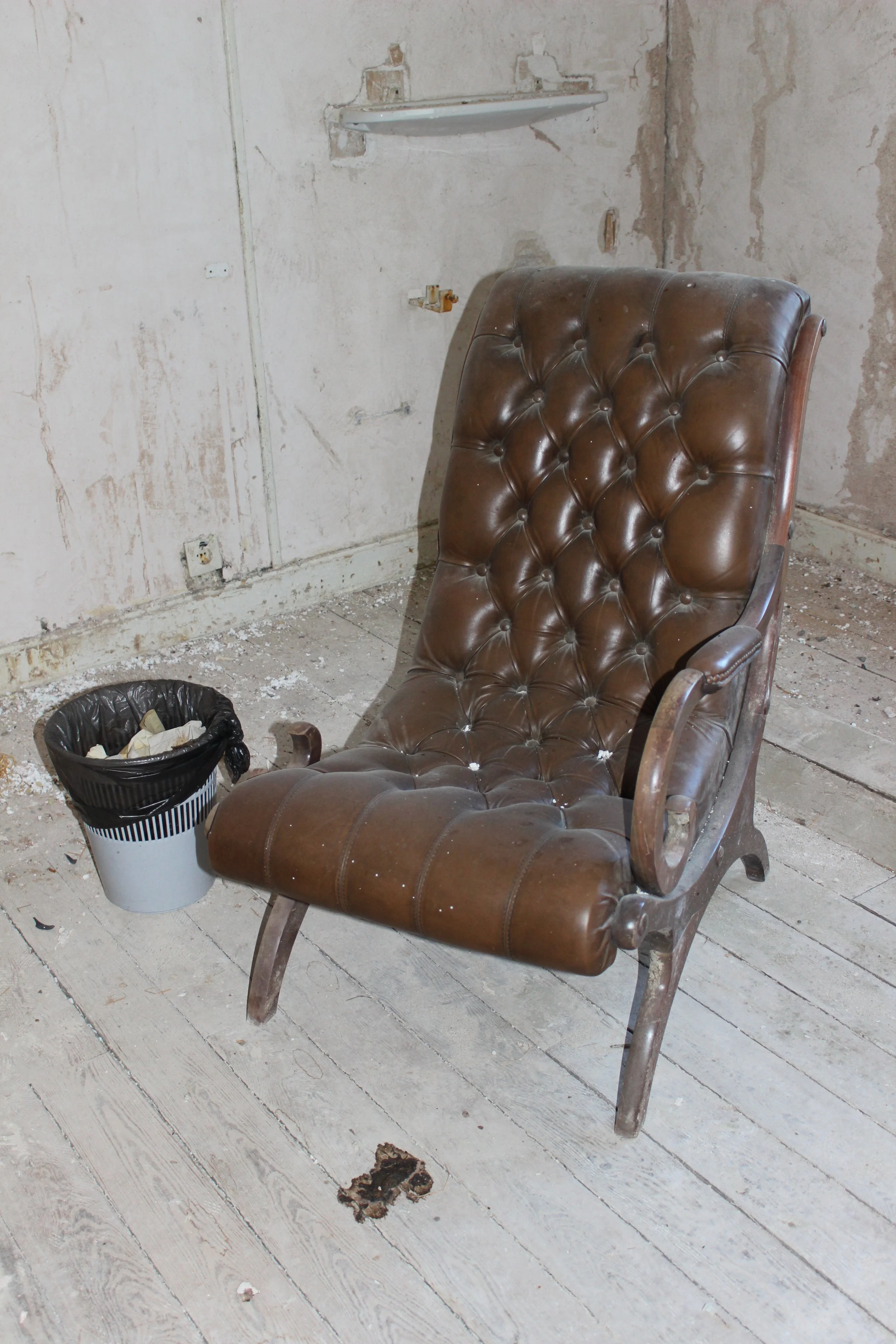 Ein alter, brauner Leder-Sessel in einem Raum, der renoviert wird, neben einem Mülleimer mit Papier.