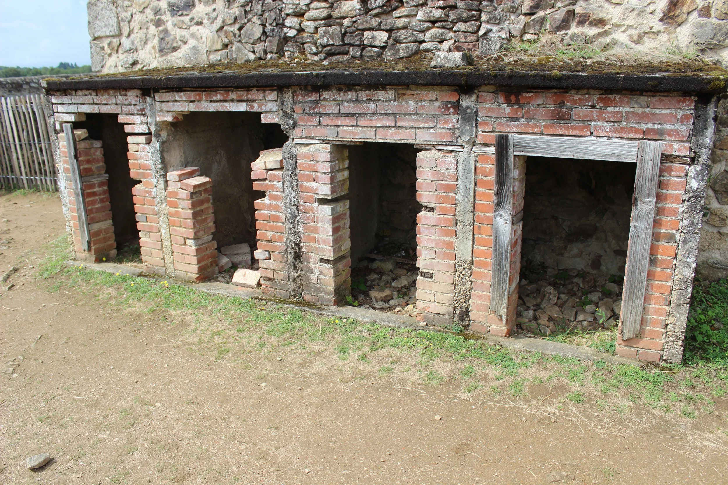 Alte, verfallene historische Feuerstellen oder Herde aus Backstein mit drei offenen Kammern, teilweise mit Ablagerungen und Steinen gefüllt, vor einer Steingrundwand.