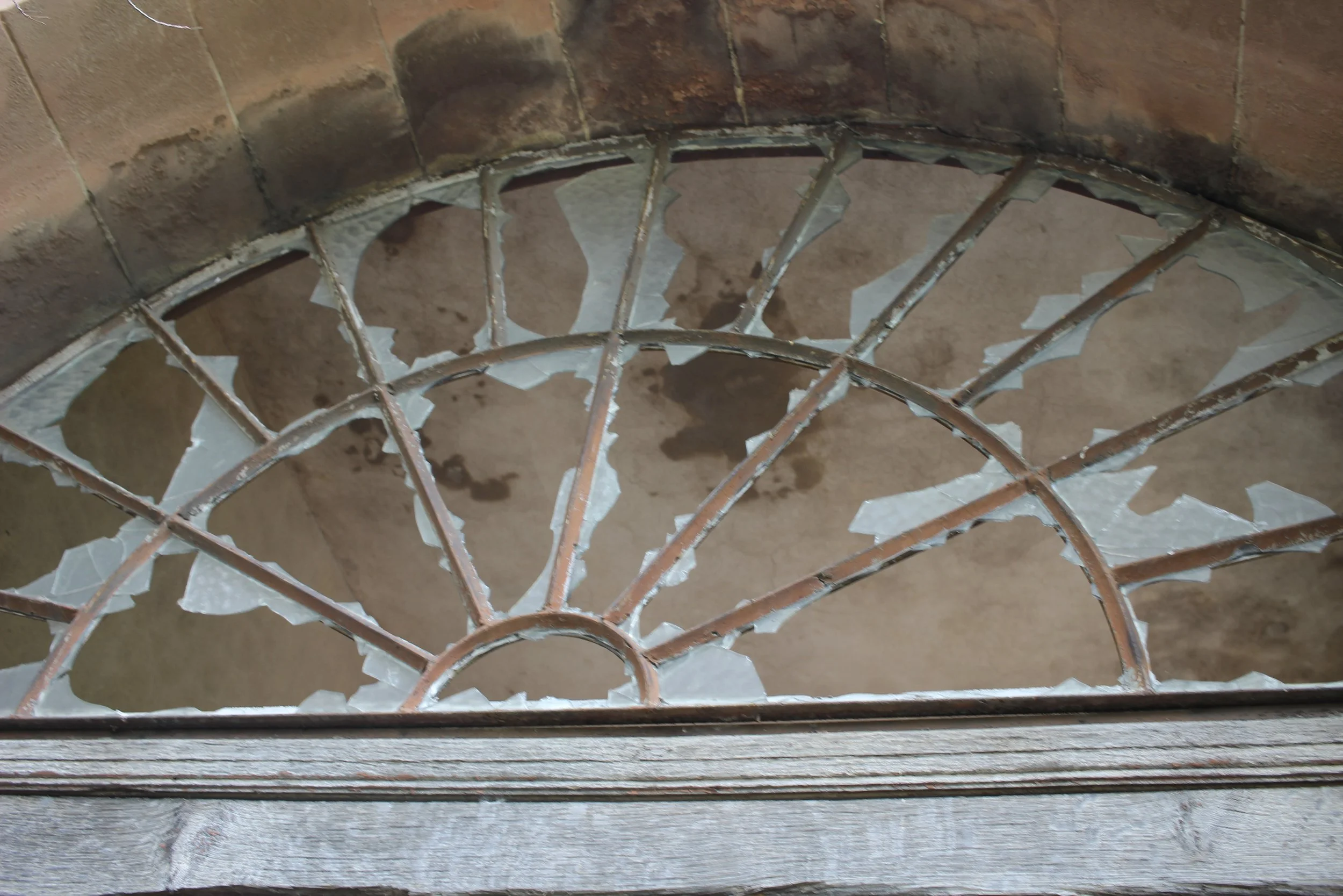 Sicht auf eine alte, zerbrochene Glasscheibe in einem rechteckigen Rahmen, die in einem Wandbogen einer Treppe eingebaut ist.