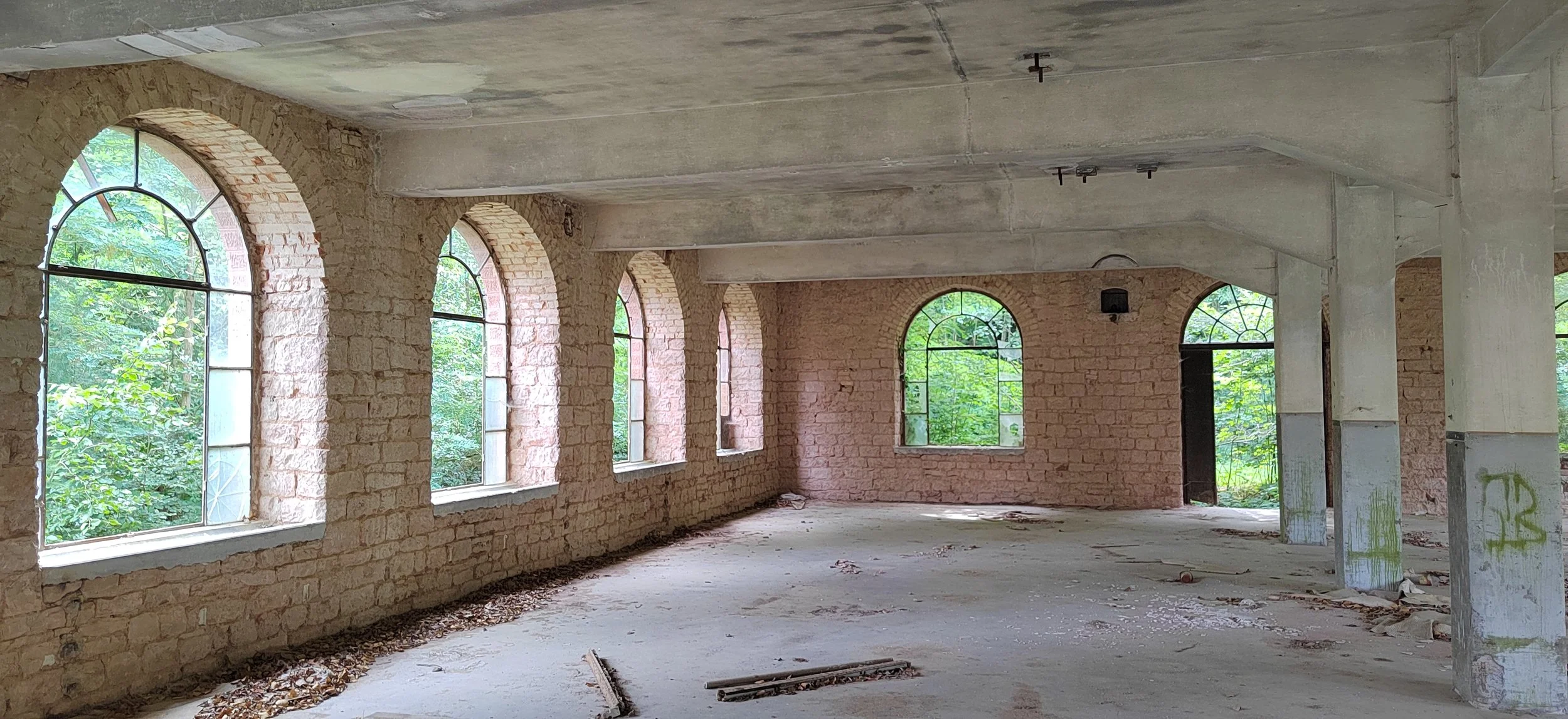 Innenansicht eines unvollendeten Gebäudes mit großen, bogenförmigen Fenstern und sichtbaren Backsteinwänden.