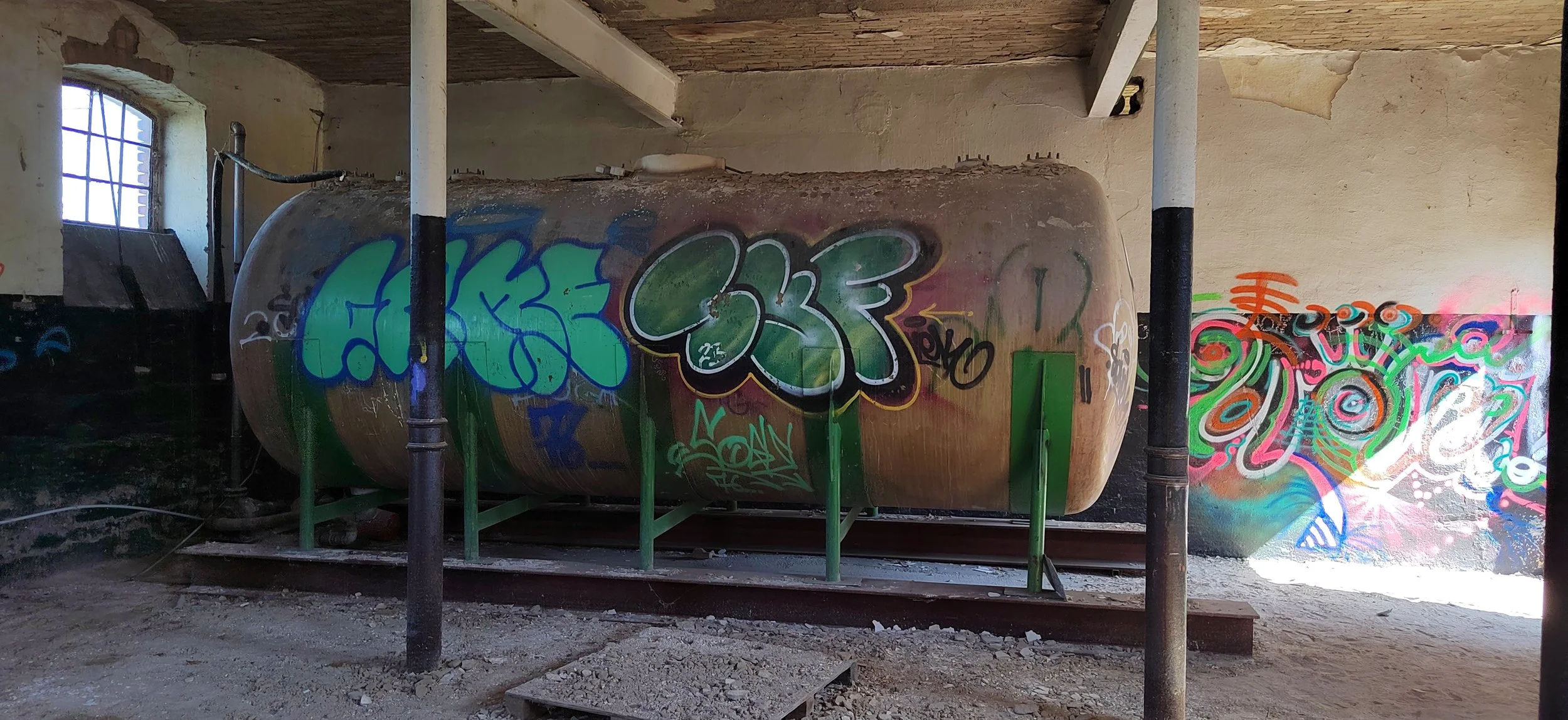 Graffiti auf einer alten, rostigen Tankstation im Inneren eines Gebäudes mit bedingtem natürlichem Licht durch ein Fenster auf der linken Seite.