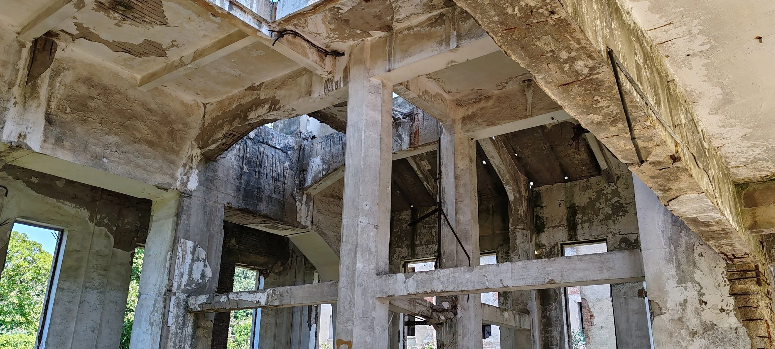 Baufassade eines alten, bröckelnden Gebäudes mit offenen Fenstern und Sicht auf die Struktur im Inneren, das durch Abnutzung und Verfall gezeichnet ist.