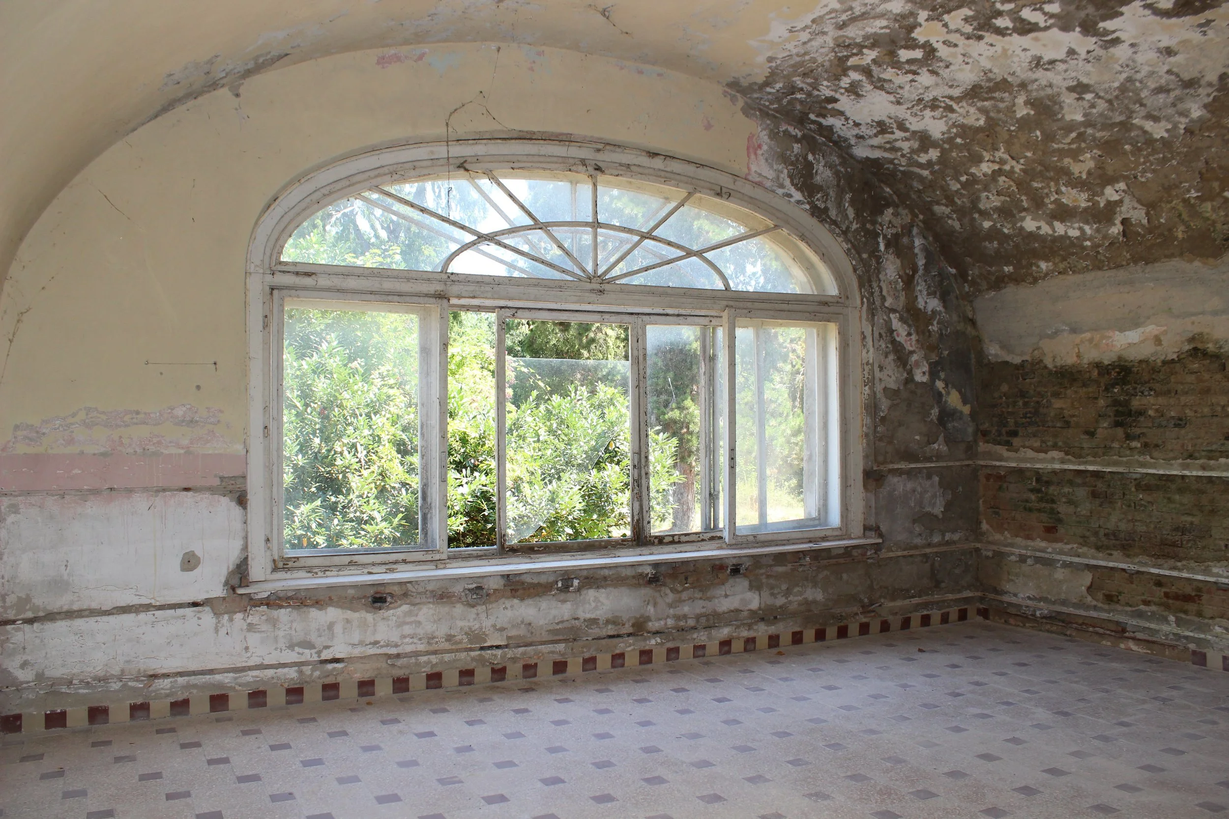 Alter, verfallener Raum mit großen Fenster, bröckelige Wände und abgenutztem Boden.