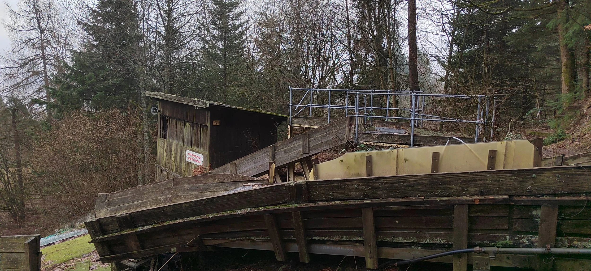 Alte Holzbeteilig im Wald mit einem Holzsteg und einem kleinen angeschlossenen Gebäude