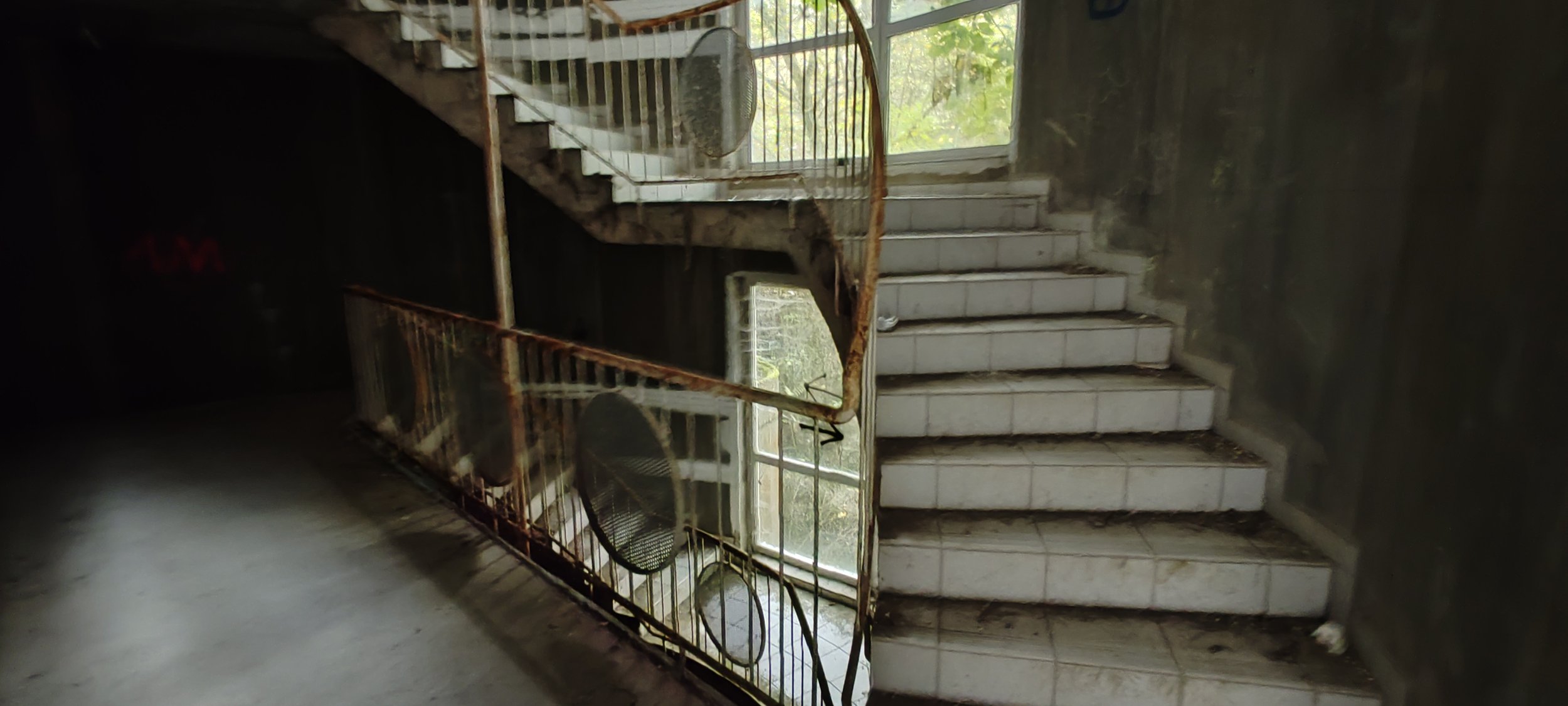 Verrostete Treppe in einem alten Gebäude mit Glasfenster im Hintergrund.