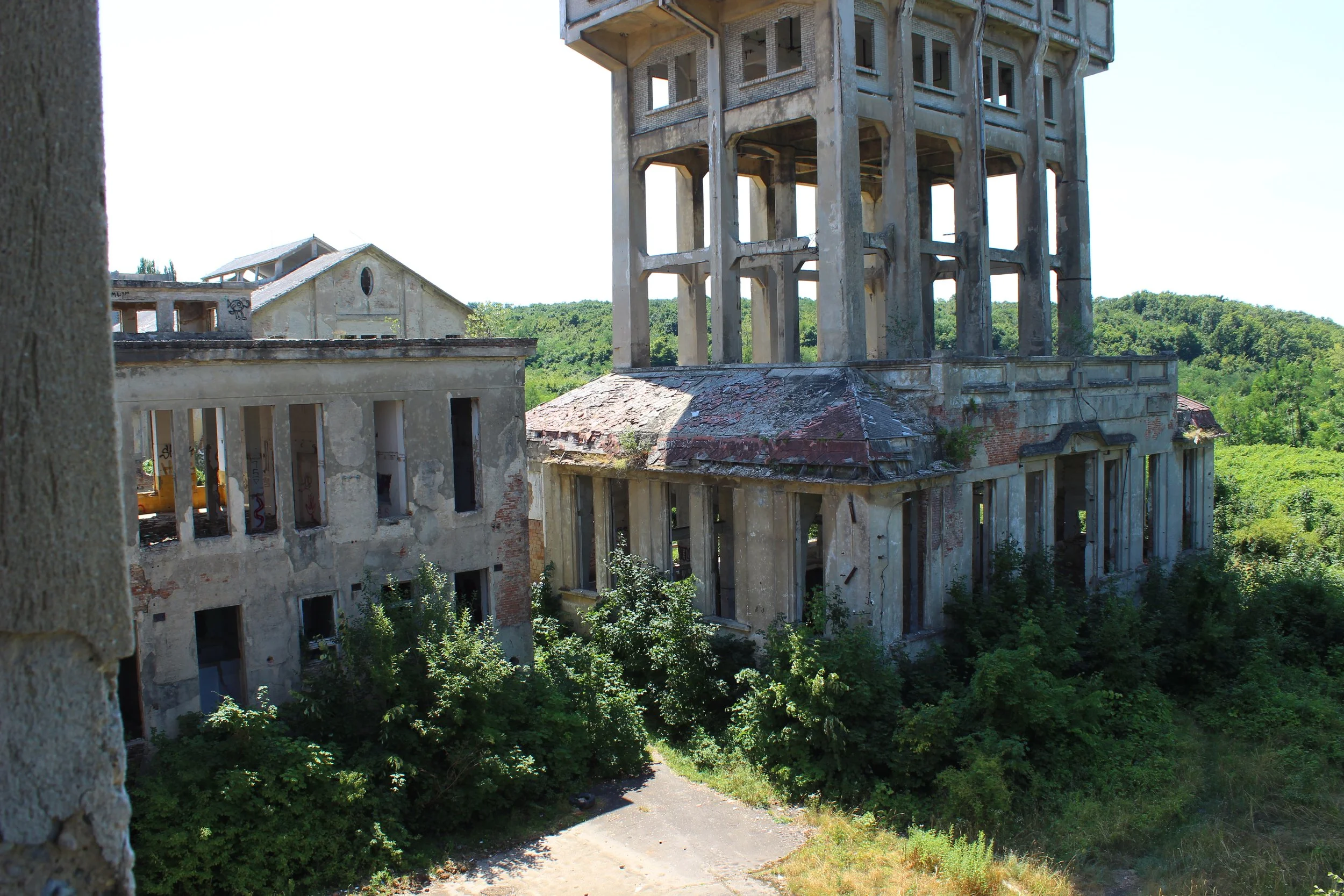 Verfallene, baufällige Gebäude mit überwachtem Turm in einer grünen Landschaft.