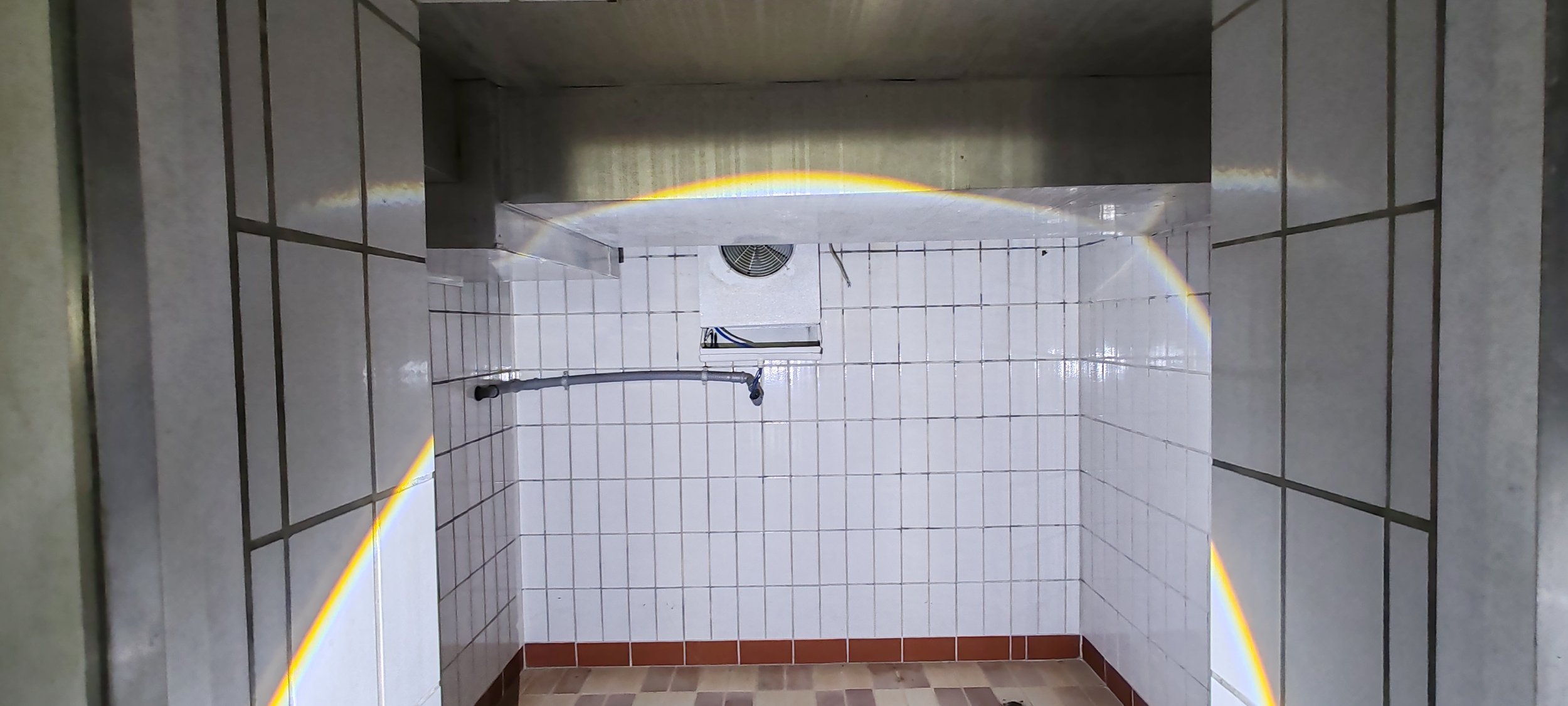 Badezimmer mit weißen Fliesen, einer Duscharmatur und einem Abluftventilator an der Wand.