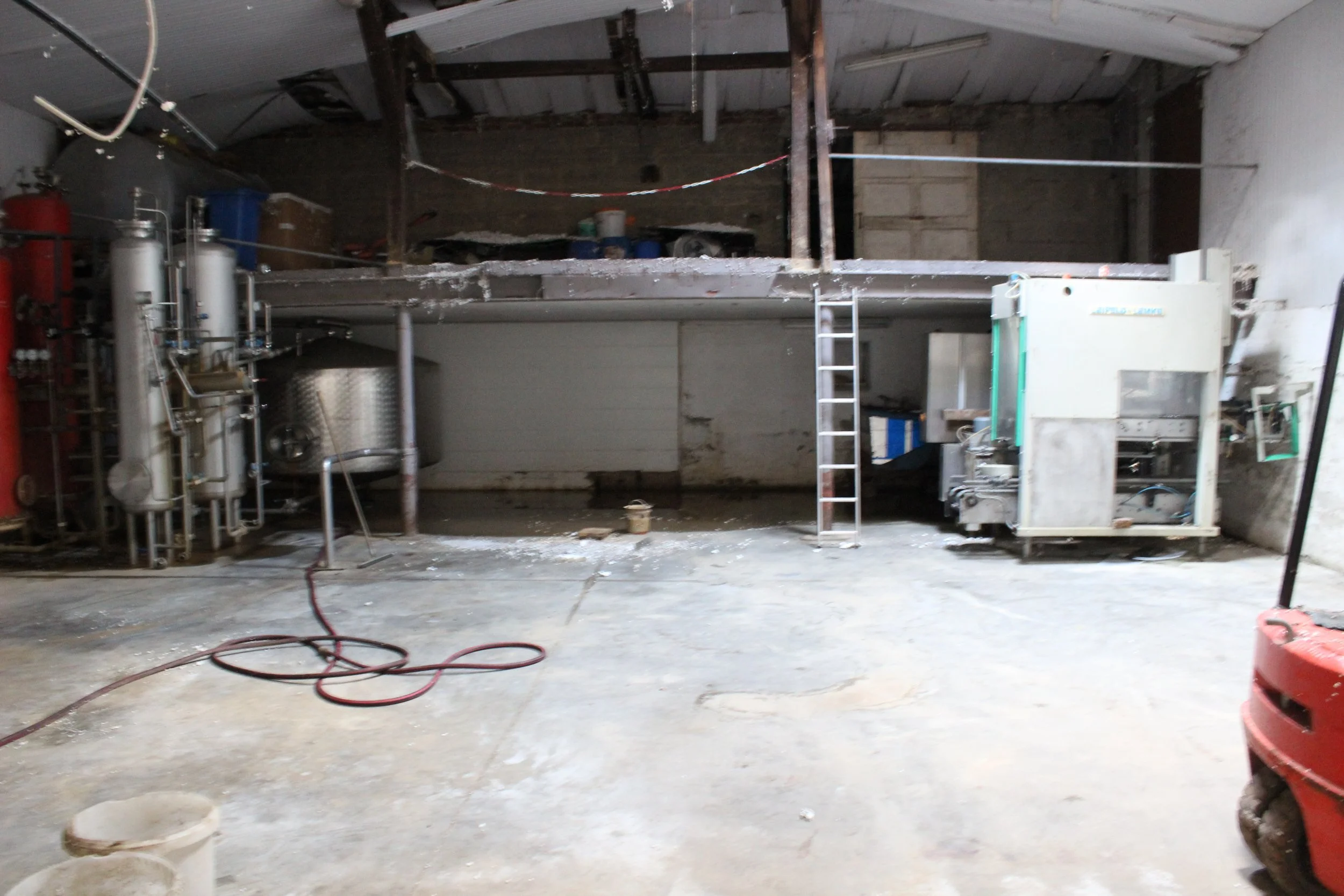 Ein unordentlicher, alter Lagerraum mit technischen Apparaturen, einer Leiter und einer schmutzigen, unebenen Betonbodenfläche.