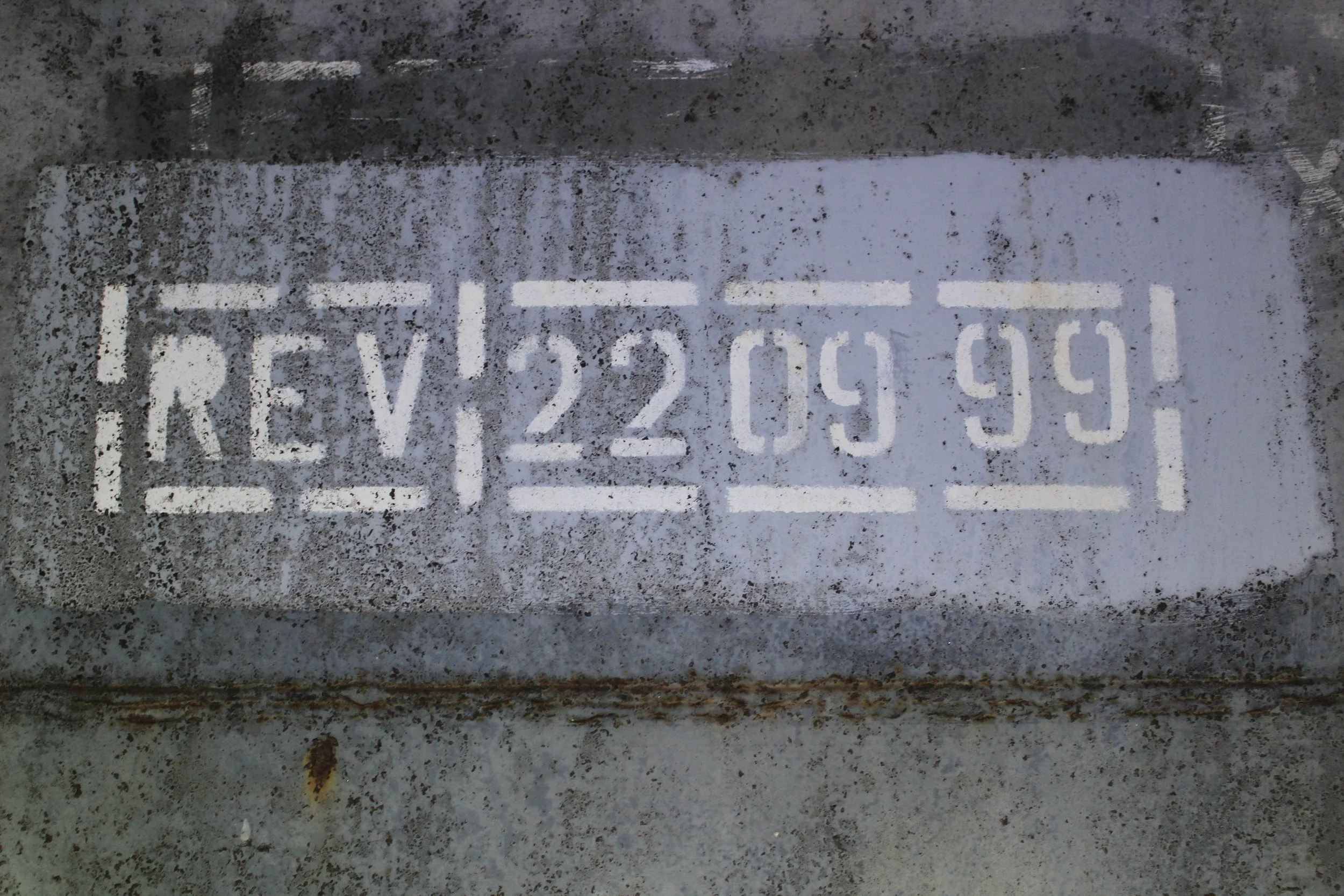 Straßenmarkierung mit der Nummer RE V 22 049 99 auf einer nassen Asphaltstraße.