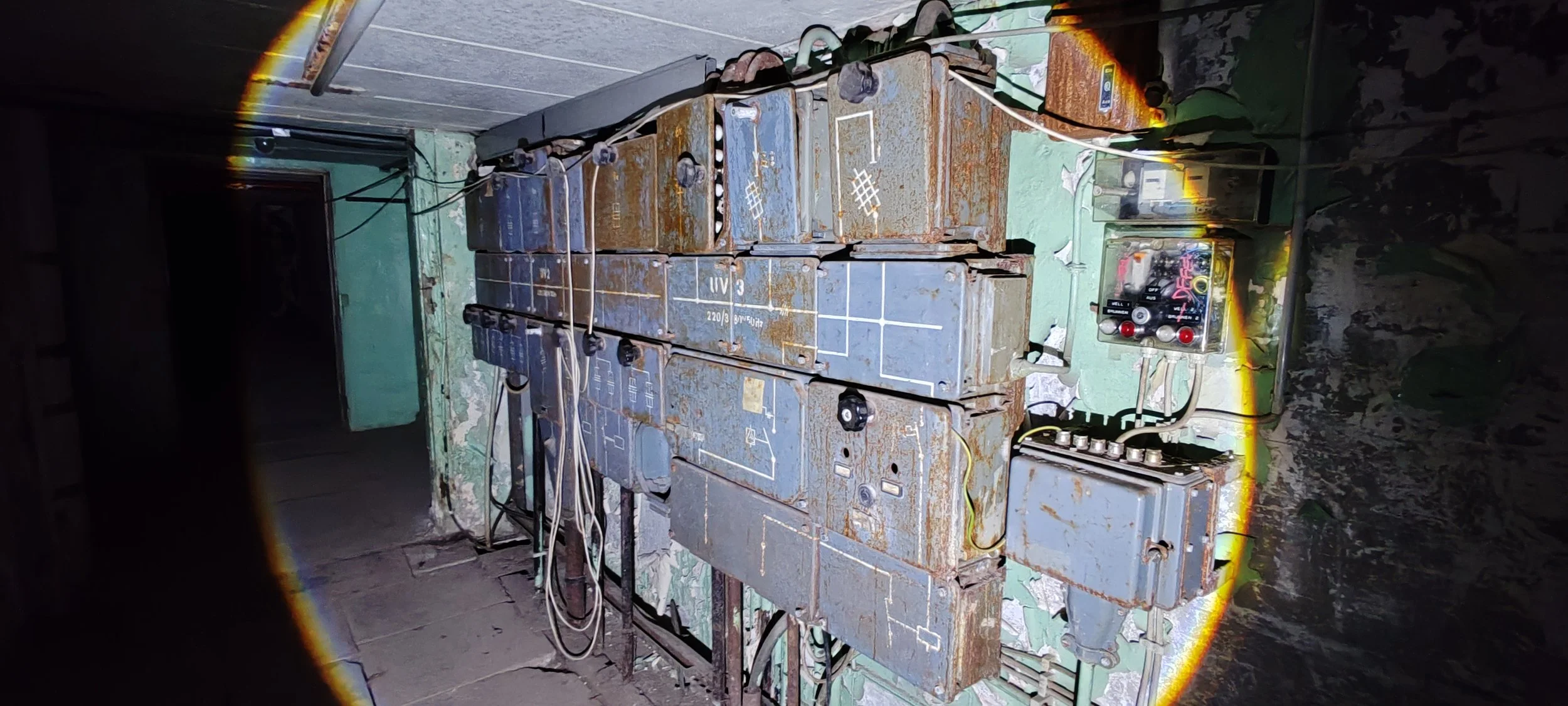 Altertümliche elektrische Steuerungskasten mit rostigen Metallkästen, verbunden mit Kabeln und einem Steuergerät in einem dunklen Raum.