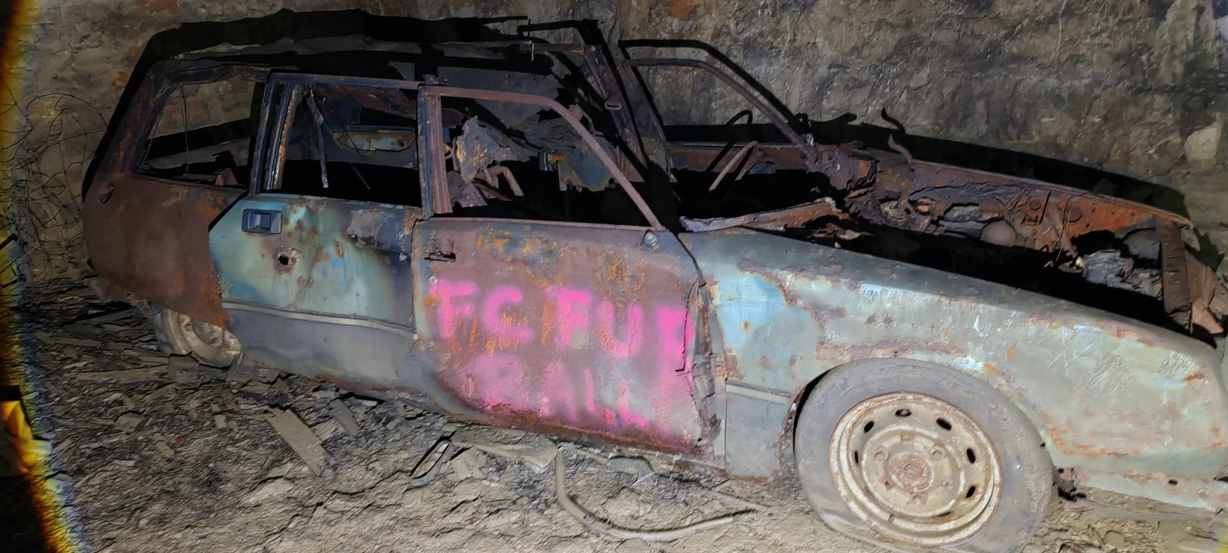 Verrosteter, beschädigter Auto-Rumpf in einem abgebrochenen Zustand, auf einem felsigen Boden, mit Graffiti auf der Tür.