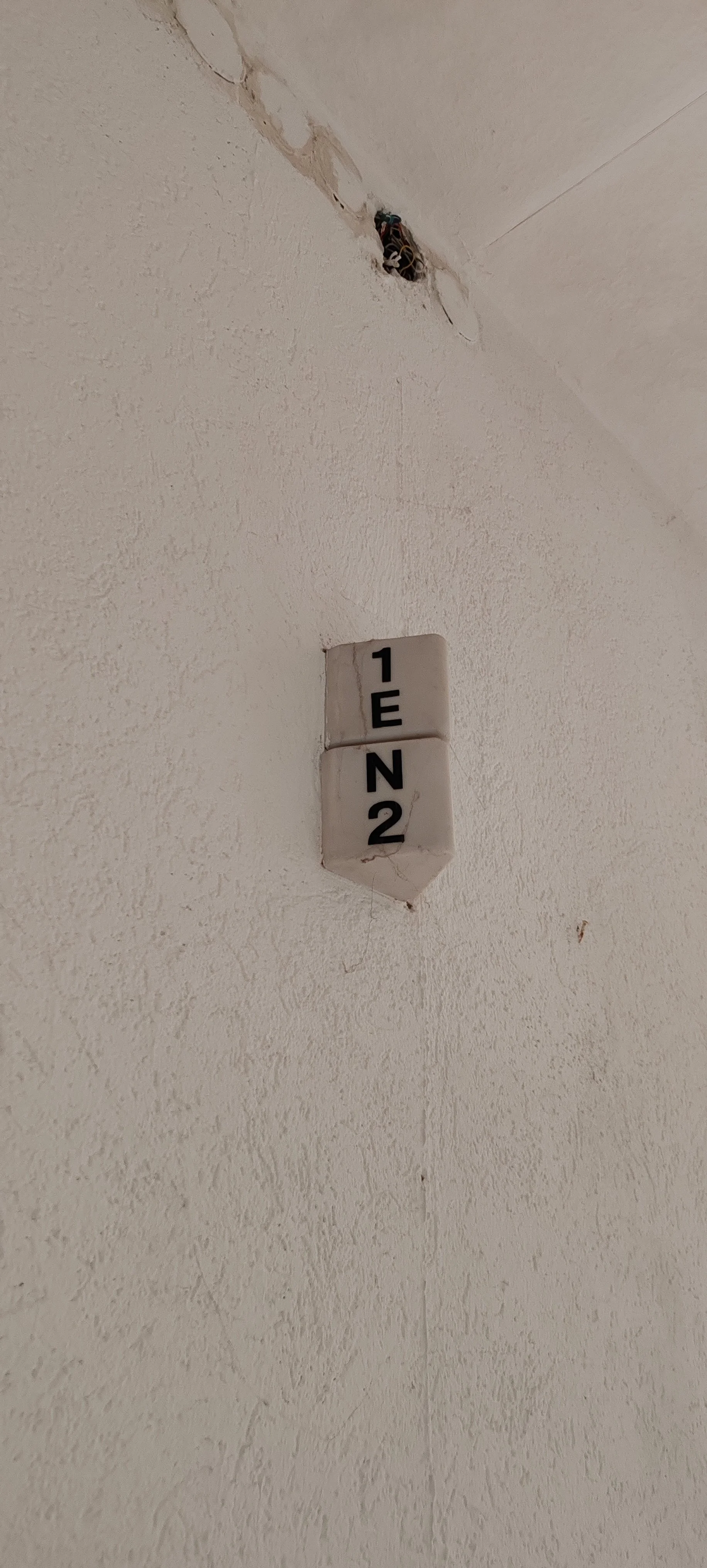 Ein Wandstück mit einer schwarzen Kabeldose und einem nummerierten Fliesenschild mit der Beschriftung '1E' und '2N'.