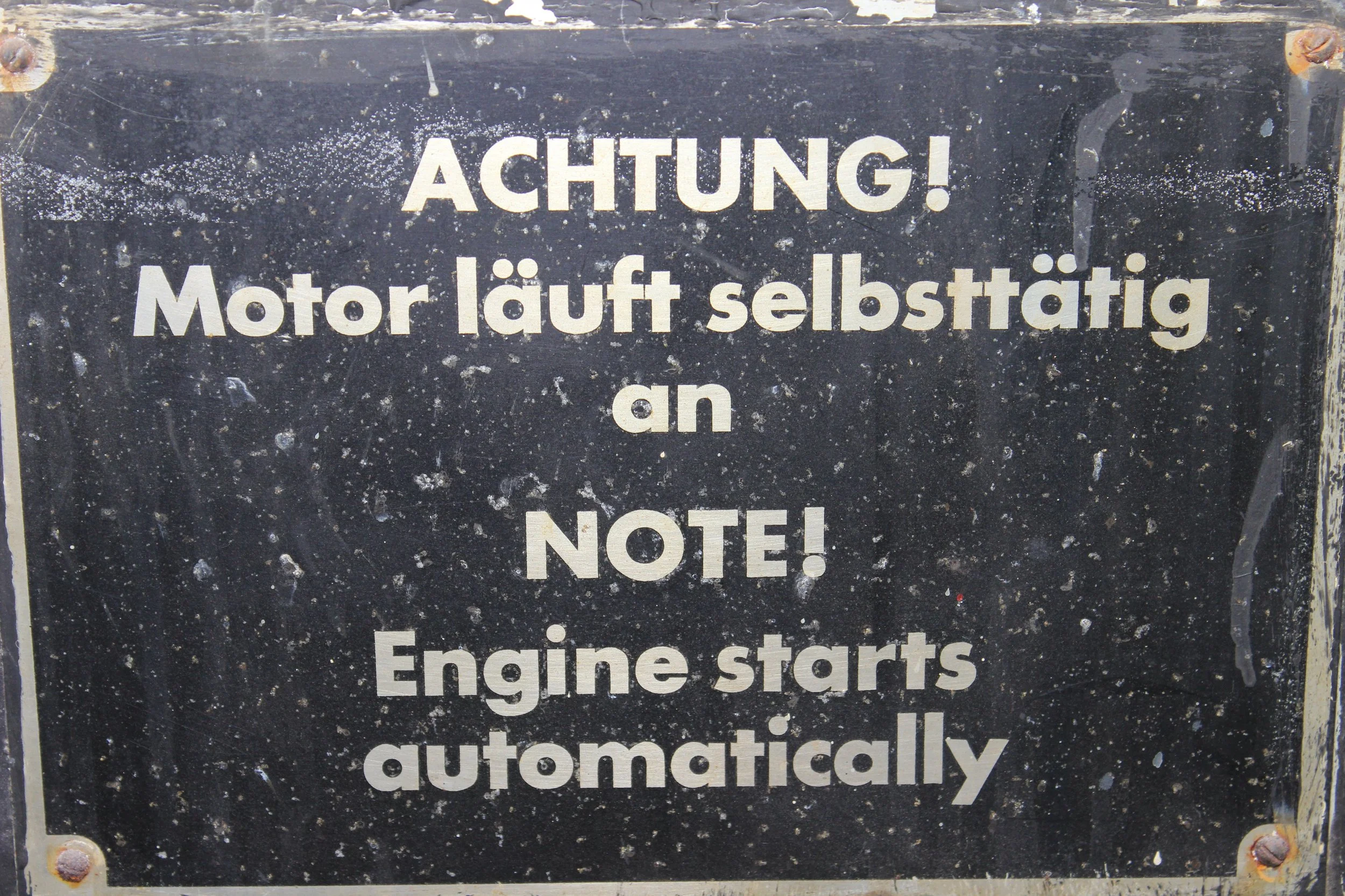 Hinweisschild mit der Aufschrift: Achtung! Motor läuft selbstständig an an Note! Engine starts automatically