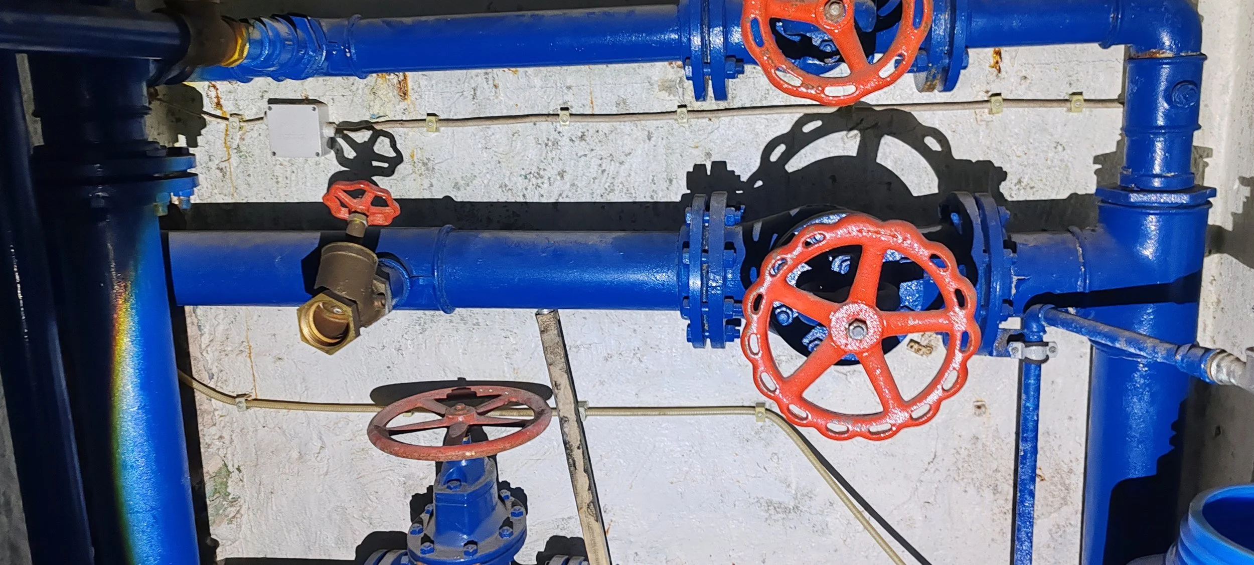 Blaue Wasserrohre mit roten Ventilen und Handrädern an einer weißen Wand