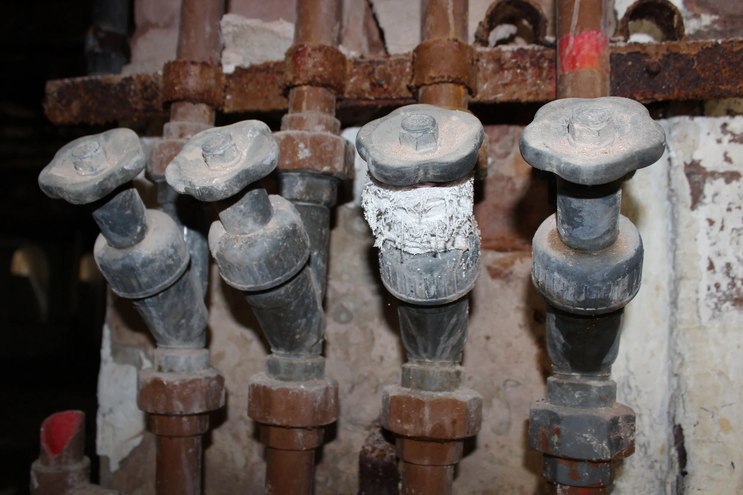 Drei große industrielle Schrauben mit Muttern, an einer Wand befestigt, mit einer weißen, cremigen Substanz an der Mitte einer Schraube.