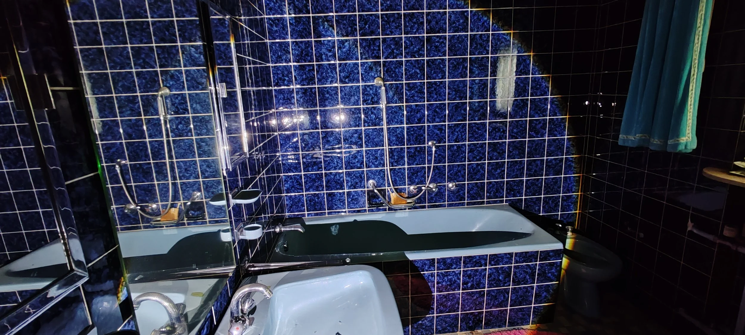 Badezimmer mit blauer Marmorfliesen, Badewanne, Waschbecken, Dusche und dunklem WC. Es gibt auch einen Spiegel und einen Handtuchhalter.