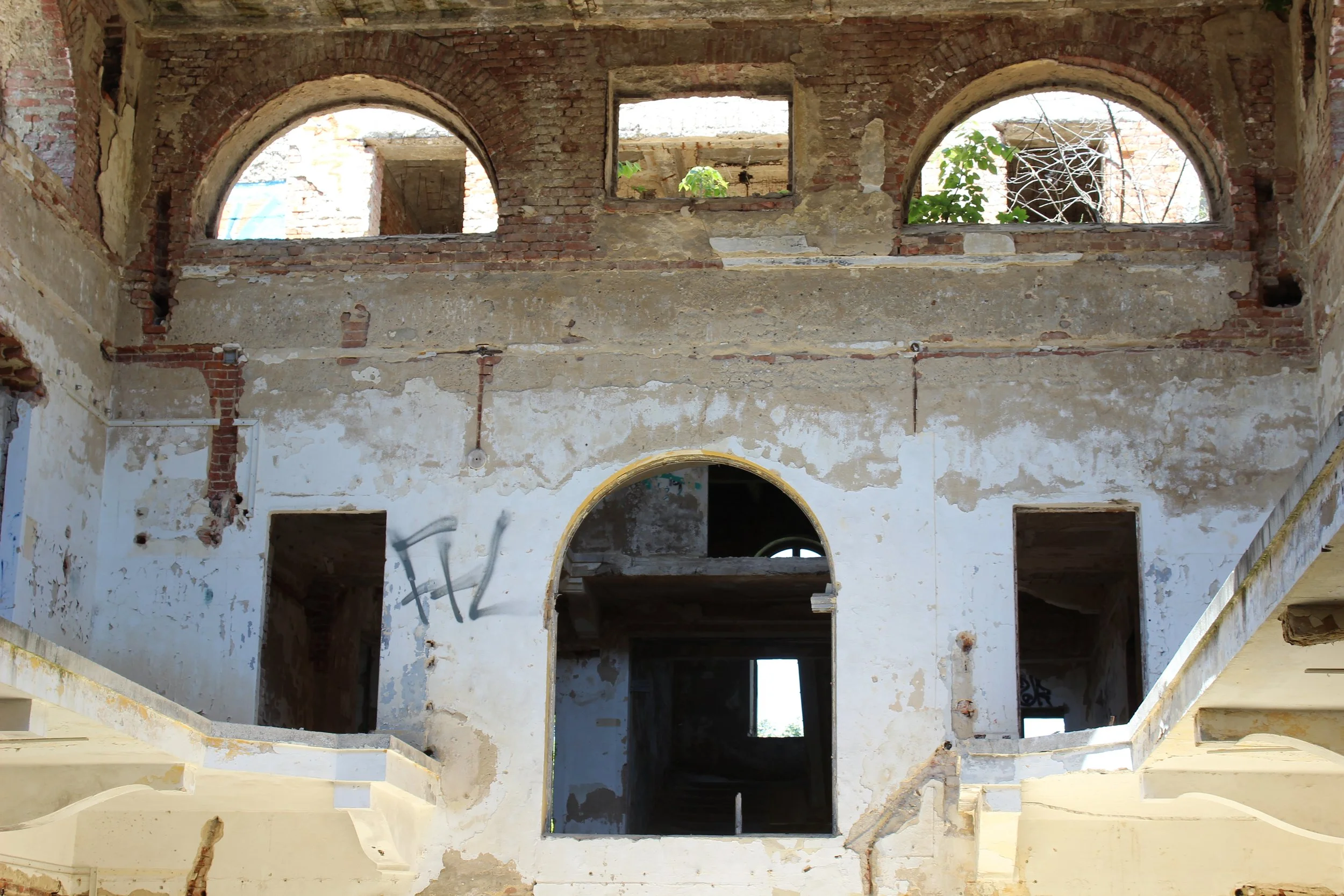 Verfallene, alte Gebäude mit offenen Fenstern und Türöffnungen, Graffiti an einer Wand, bröckelnder Putz, im Inneren sichtbare Dunkelheit und Schatten.