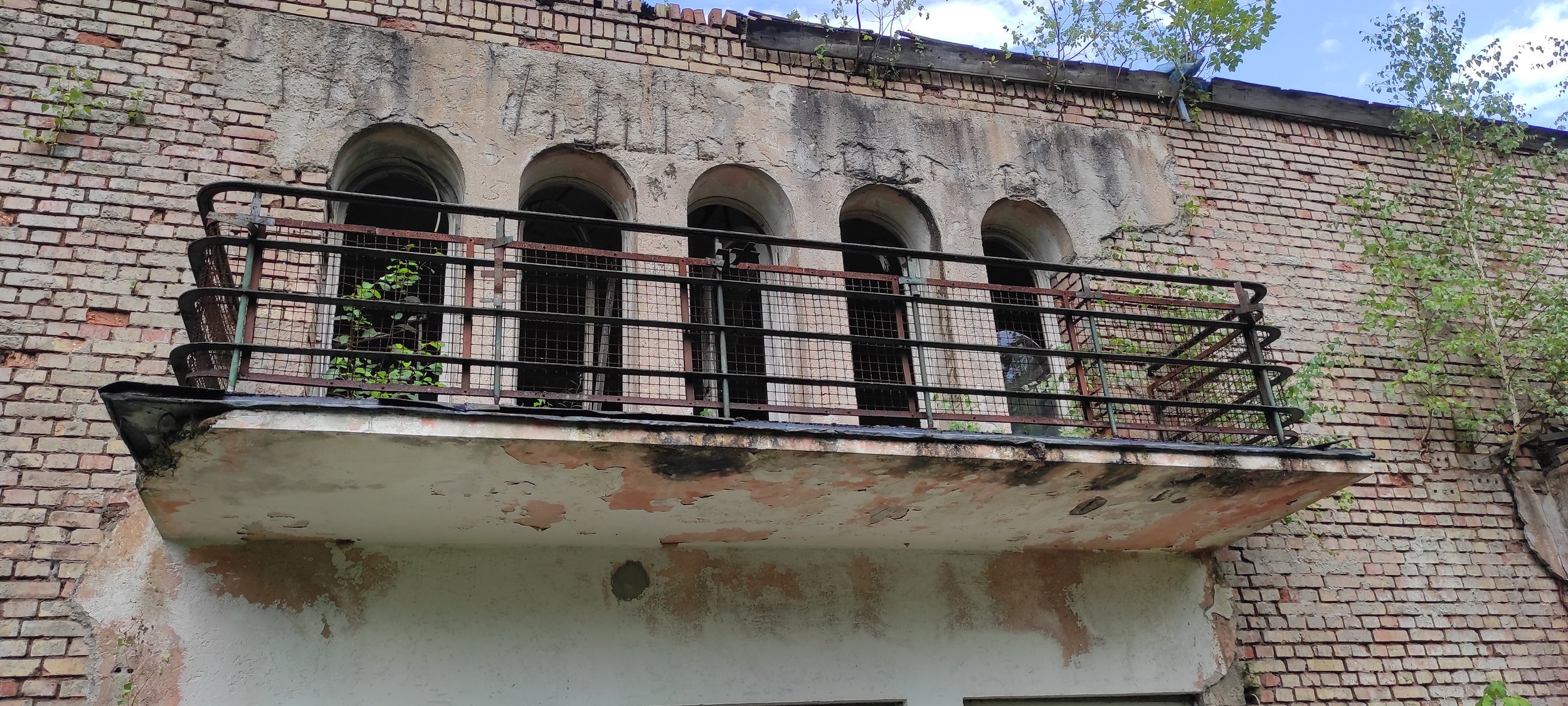 Alter Balkon mit verrostetem Geländer und bröckelnder Putzwand, an einer Backsteinmauer