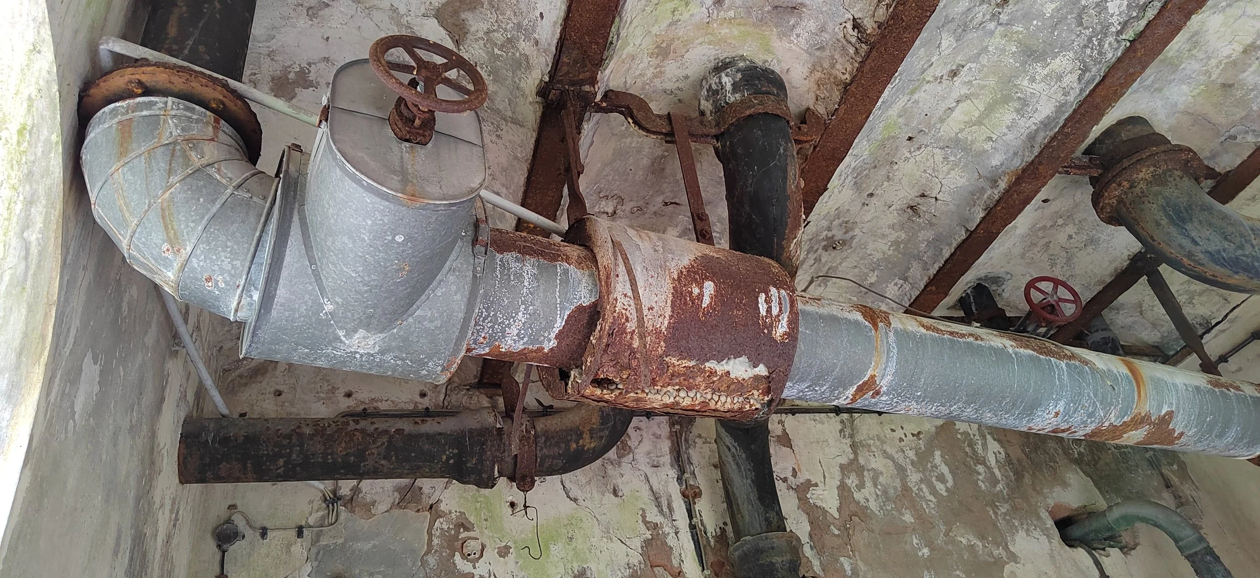 Alte verrostete Rohrleitungen und Ventile in einem Keller oder Lagerraum.