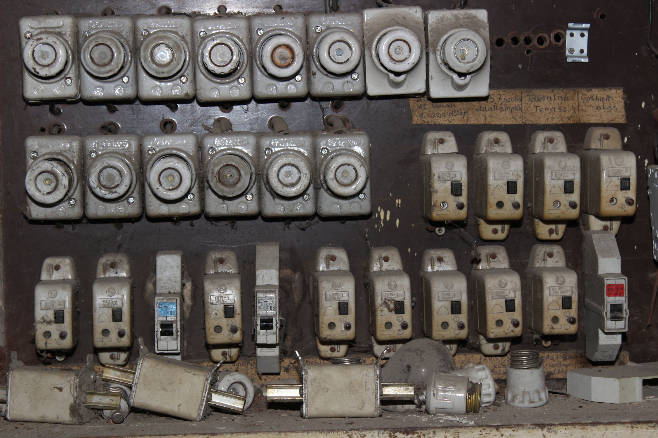 An der Wand montierte alte elektrische Schalter, Sicherungen und Verkabelung, die sichtbar verfärbt und verschmutzt sind.