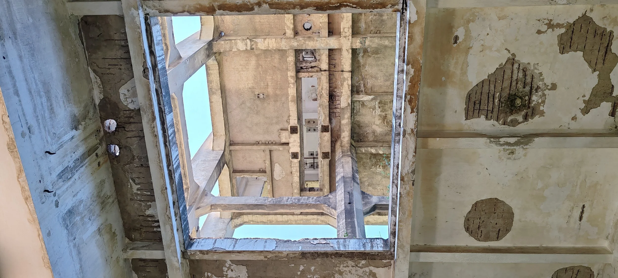 Innenansicht eines verlassenen, verfallenen Gebäudes mit beschädigten Wänden und offenen Fenstern.