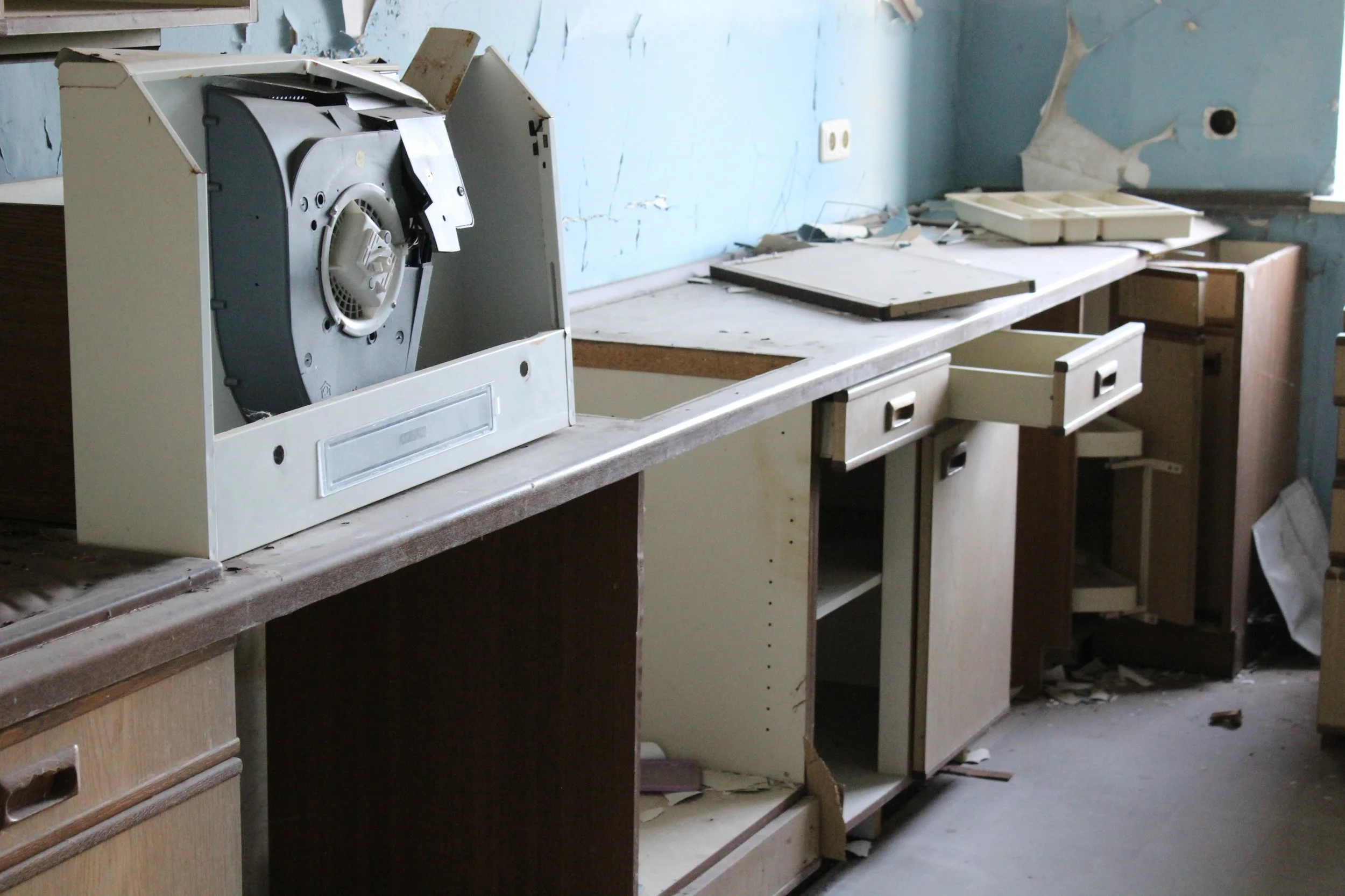 Verlassene, verfallene Küche mit beschädigten und zerbrochenen Schränken, verstreutem Staub und Schmutz auf dem Boden und zerbrochenem Inventar.