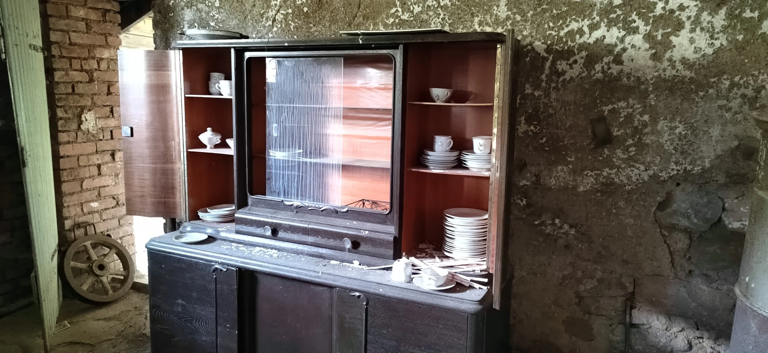 Alter Geschirr-Schrank mit Gläsern und Tellern, Staub und Staub auf der Oberfläche, kaputtes Ambiente, Stein- und Ziegelwände, verstaubtes ländliches Haus.