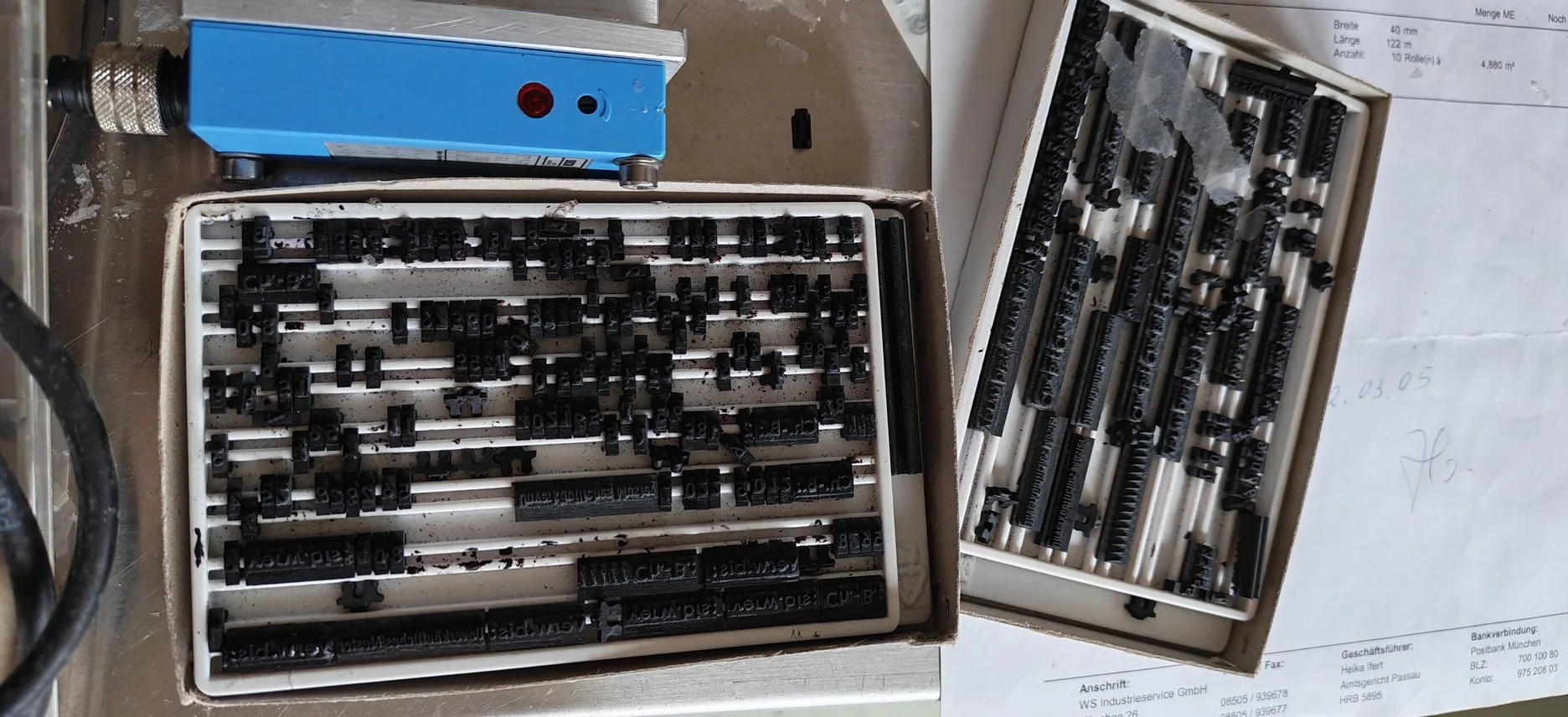 Zwei Kisten mit schwarzen Nylonschriften und Nummern auf ihnen, wahrscheinlich Schrifttypen oder Druckbuchstaben, die auf einer Werkbank liegen