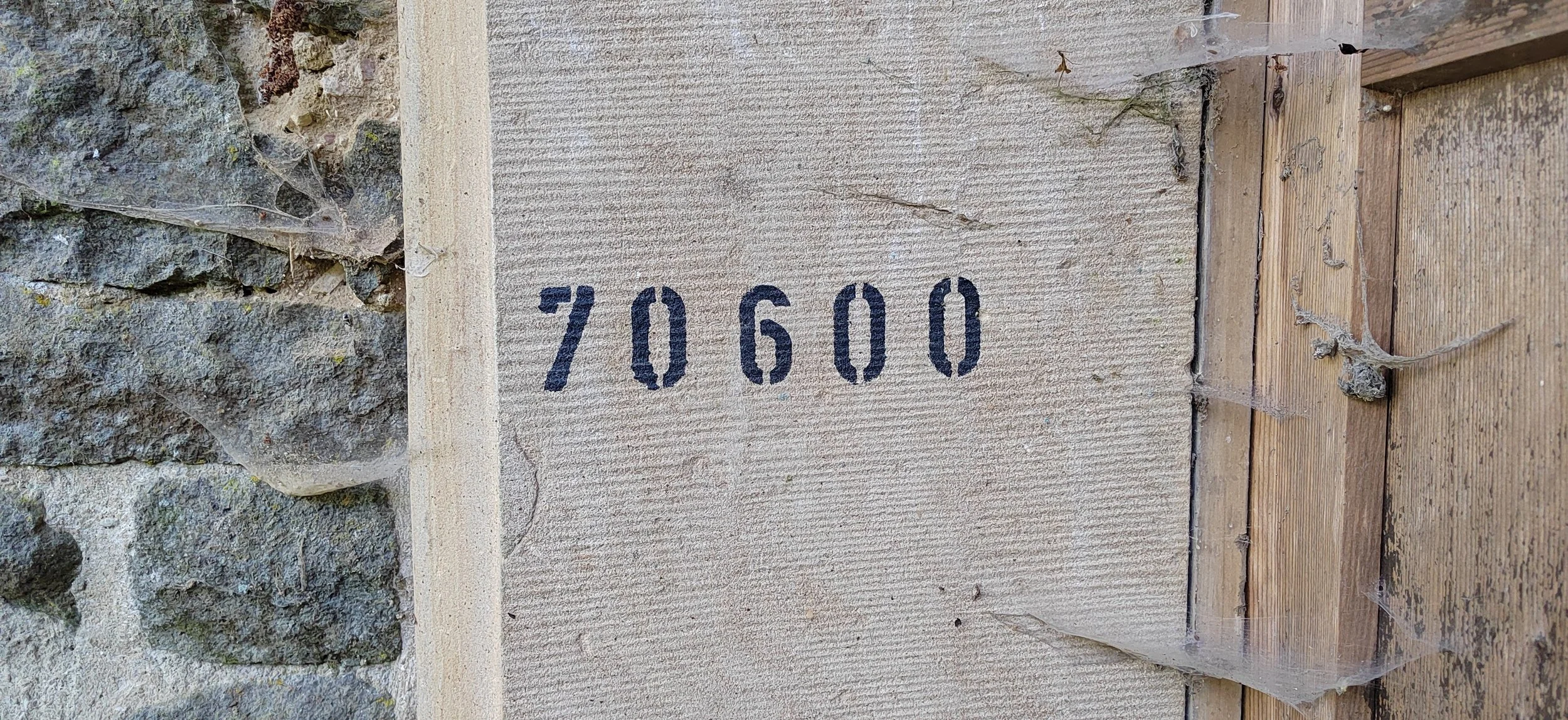 Ziegelstein mit Nummer 70600, umgeben von Holz und Steinen, verziert mit Spinnweben.