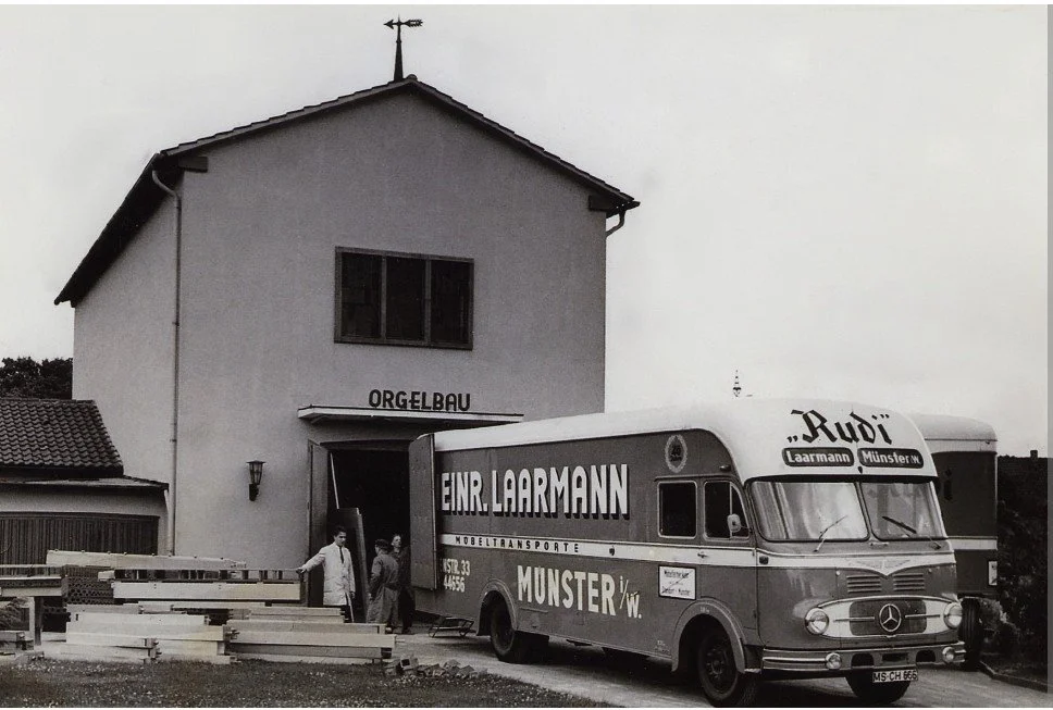 Ein historischer VW-Kastenwagen mit Werbung für Lautsprechertransporte in Münster parkt vor einem Gebäude mit der Beschriftung 'Orgelbau'; zwei Personen stehen neben dem Bus.