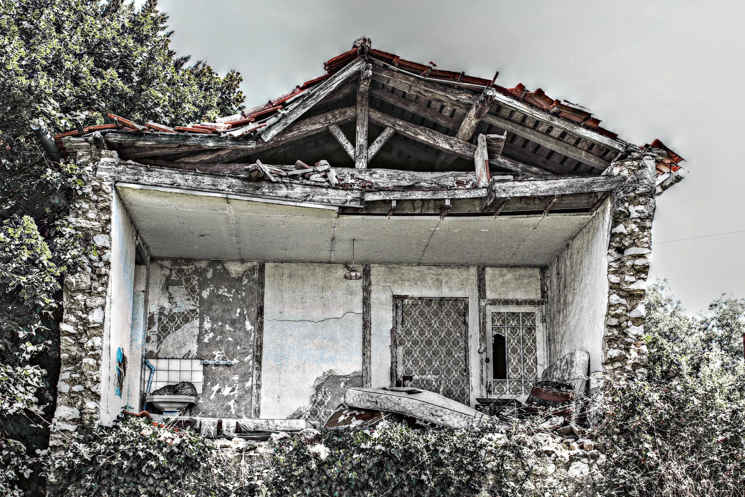 Verfallenes, beschädigtes altes Haus mit zerbrochenem Dach, zerfetztem Fenster und verwachsenen Pflanzen vor der Fassade.