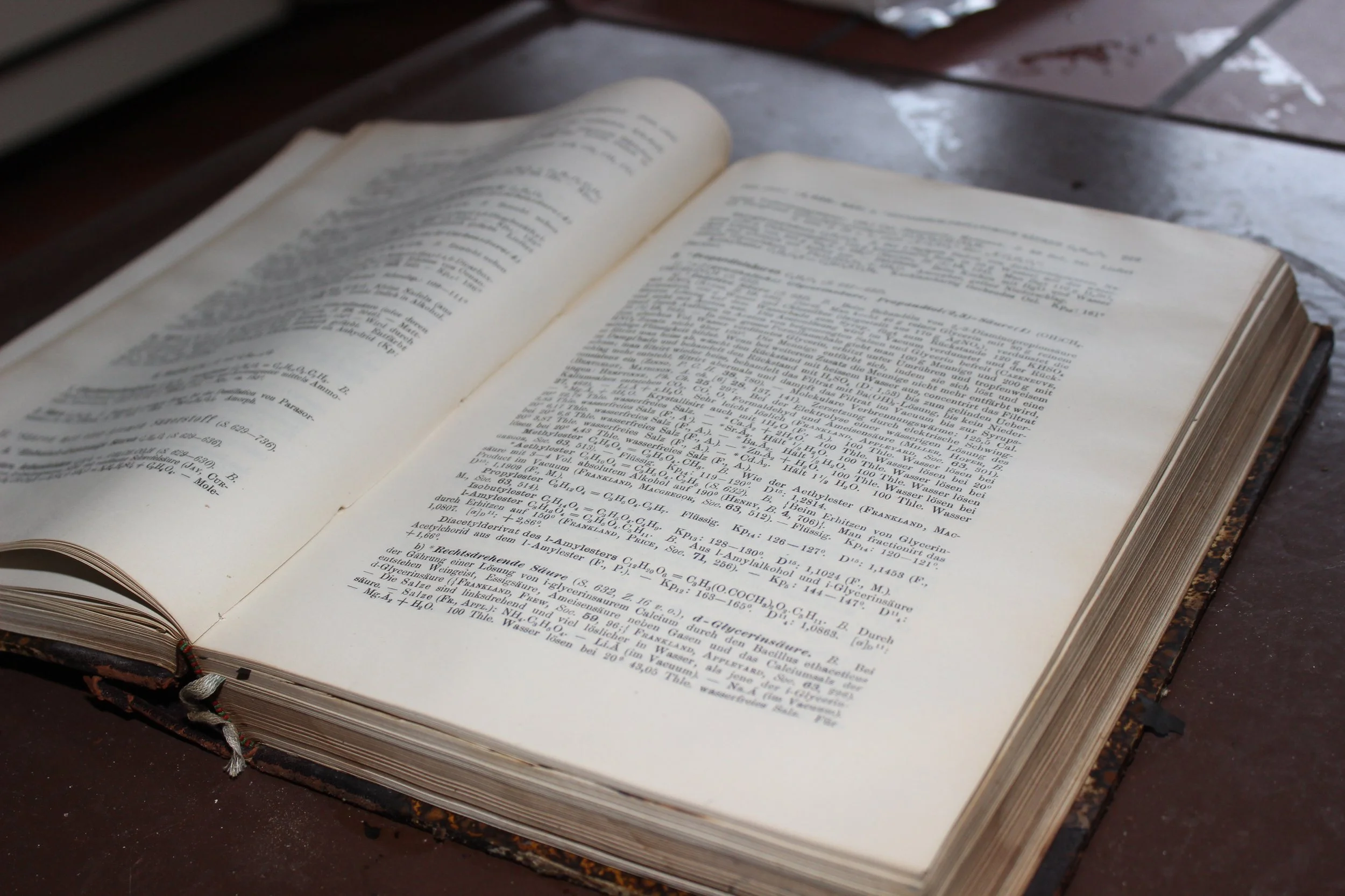 Ein offenes altes Buch liegt auf einem Holztisch, die Seiten sind mit wissenschaftlichem oder technischem Text in Deutsch gefüllt.