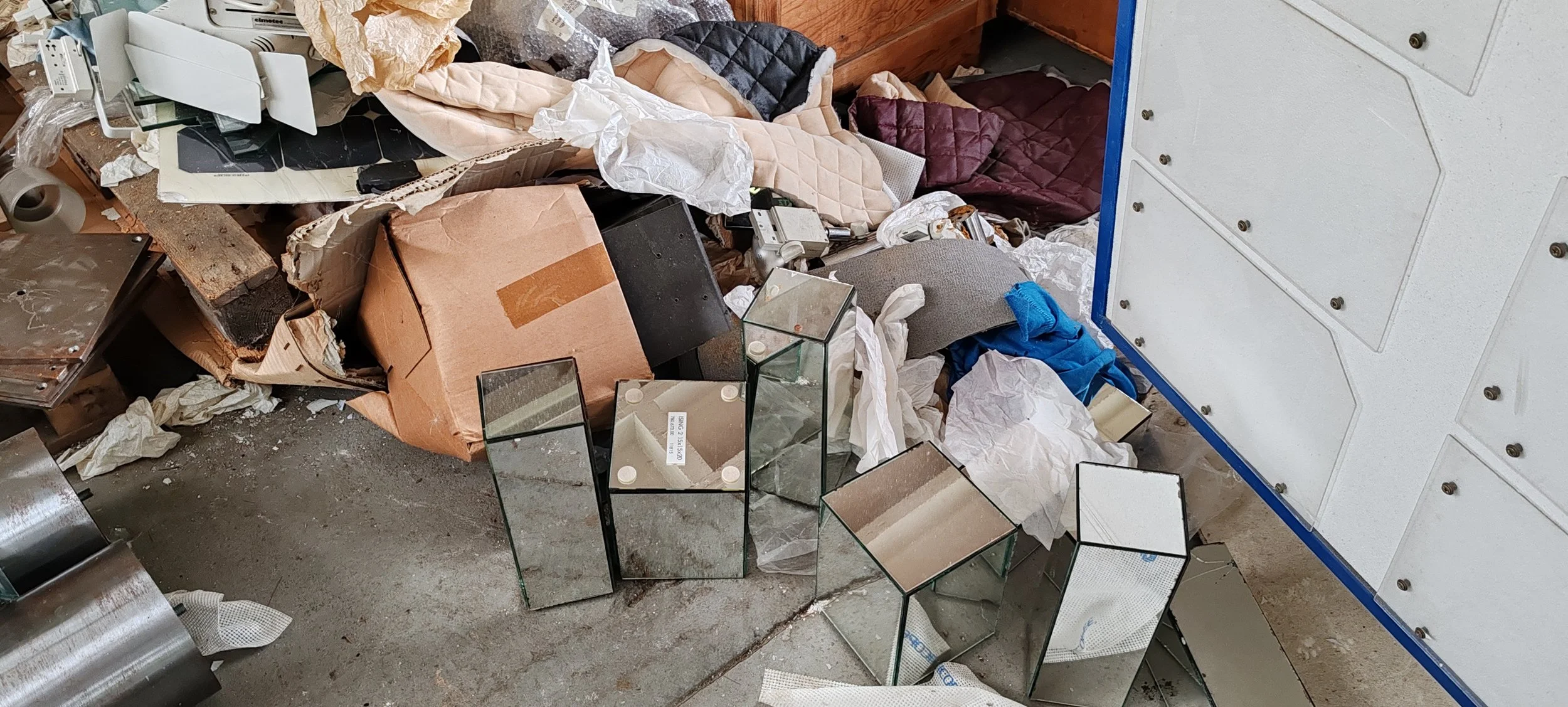 Unordentlicher Raum mit zerbrochenen Spiegeln, Papier, Kissen, Verpackungsmaterial und anderen Gegenständen