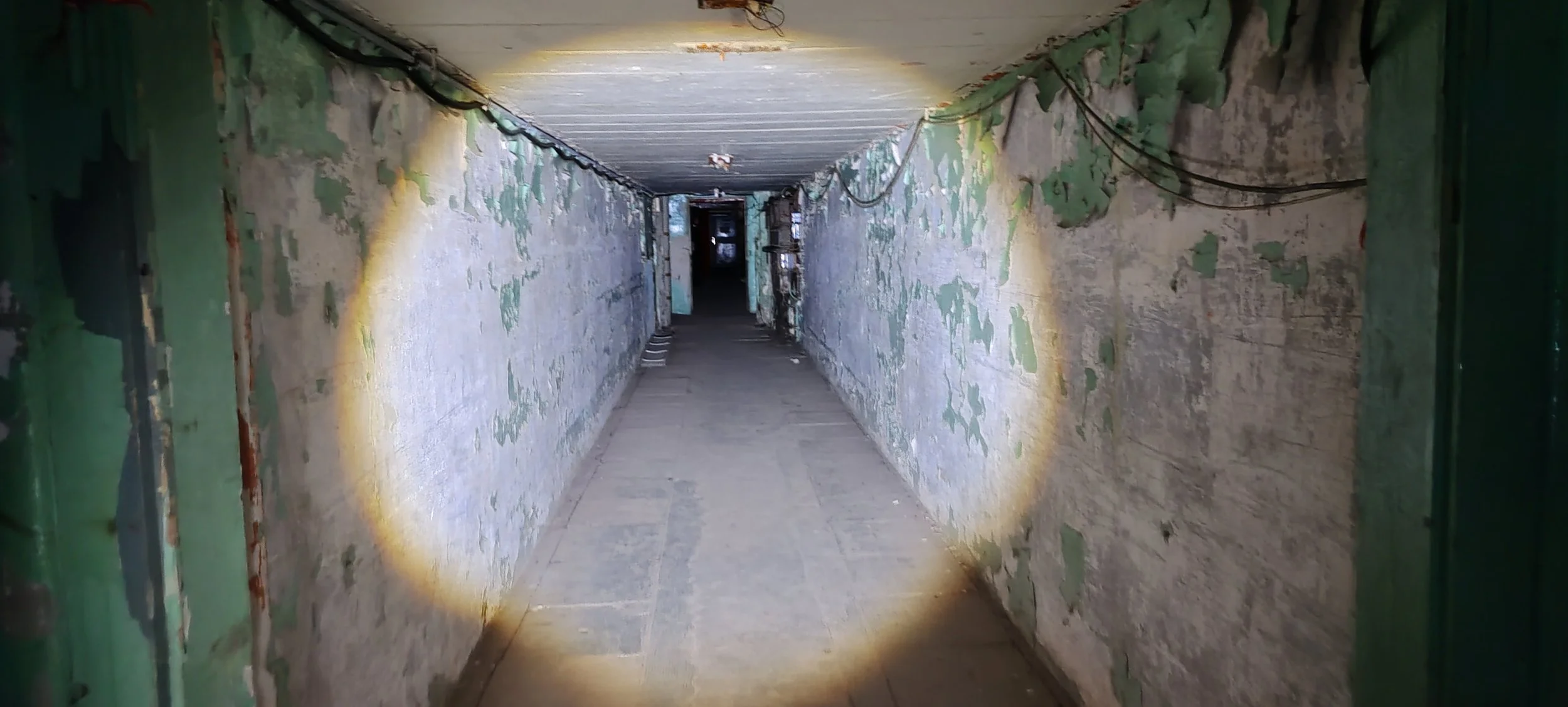 Ein dunkler, schmaler Korridor mit erhaltener, altplatierter Wandgestaltung, beleuchtet durch eine Taschenlampe.