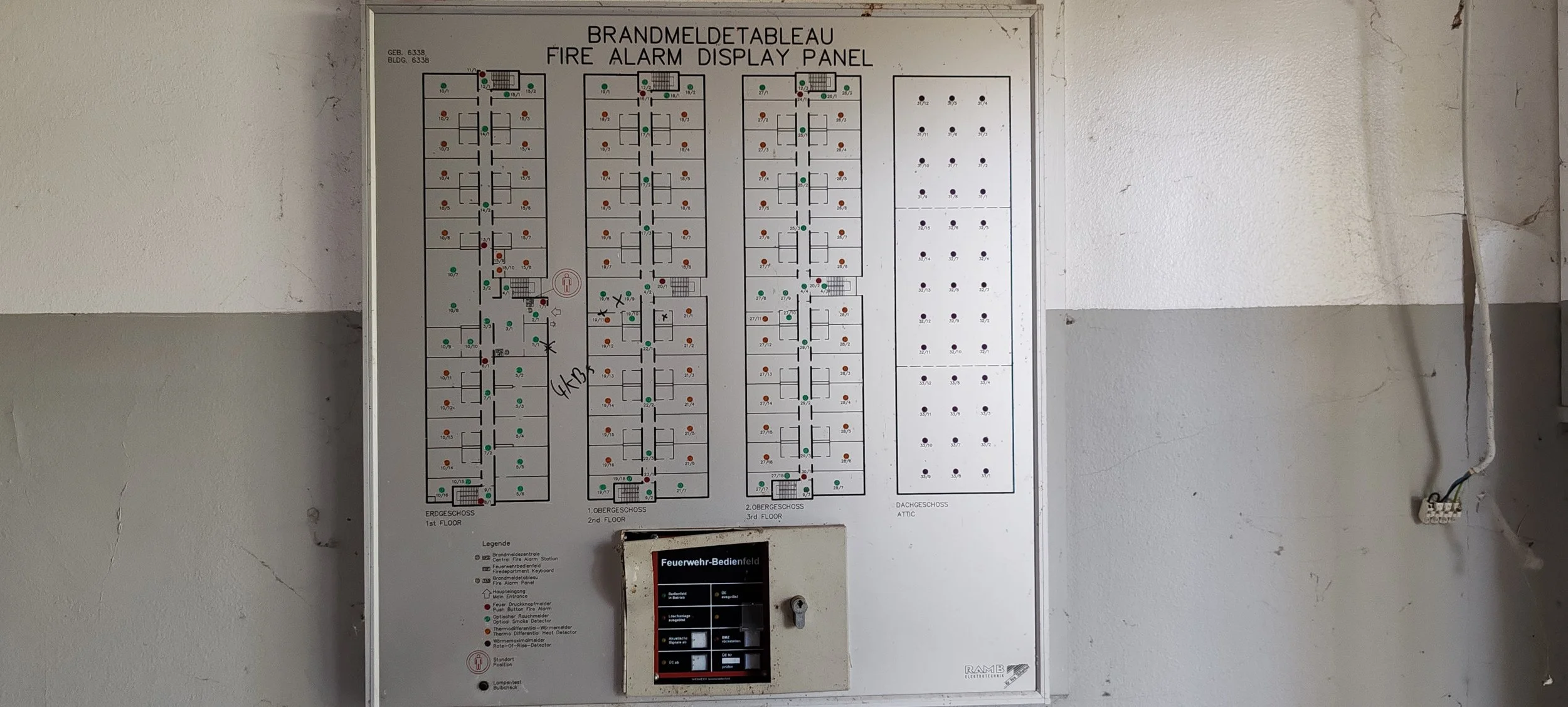 Feueralarm- und Brandmeldeplan in einem Gebäude, zeigt die Grundrisse verschiedener Stockwerke mit Statusanzeigen und einem Bedienfeld für die Feuerwehr im unteren Bereich.