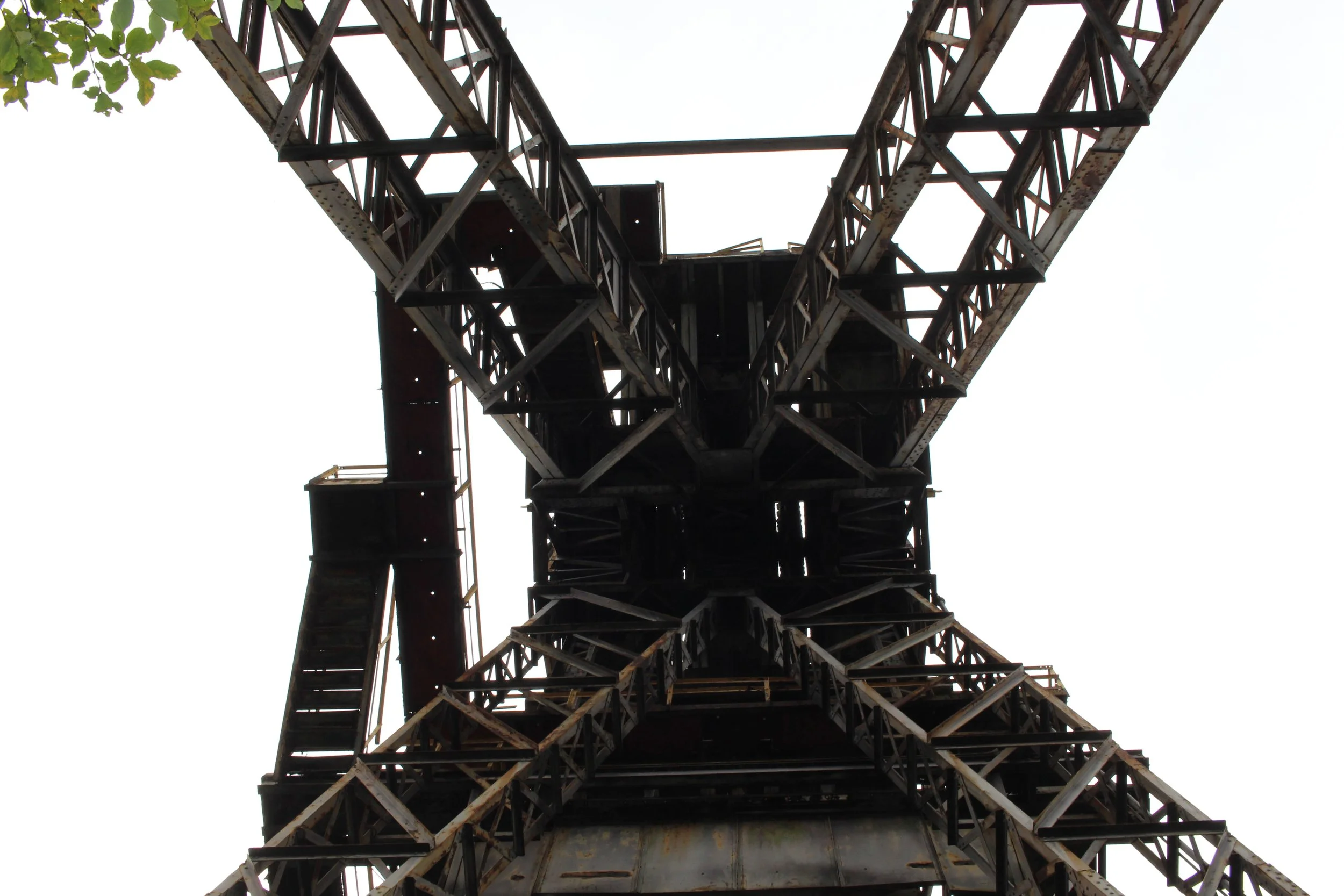 Blick nach oben auf eine alte, rostige Industrieturmstruktur mit Gitter und Plattformen.