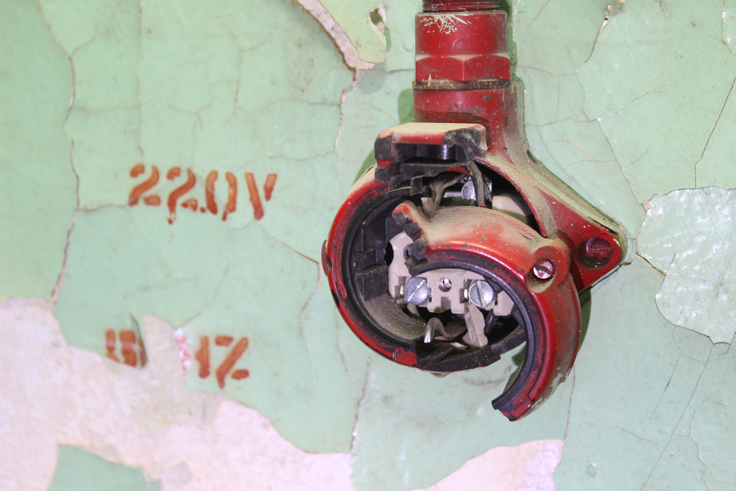 Ein zerstörter roter Elektroschalter an einer alten, abblätternden Wand mit grüner Farbe.