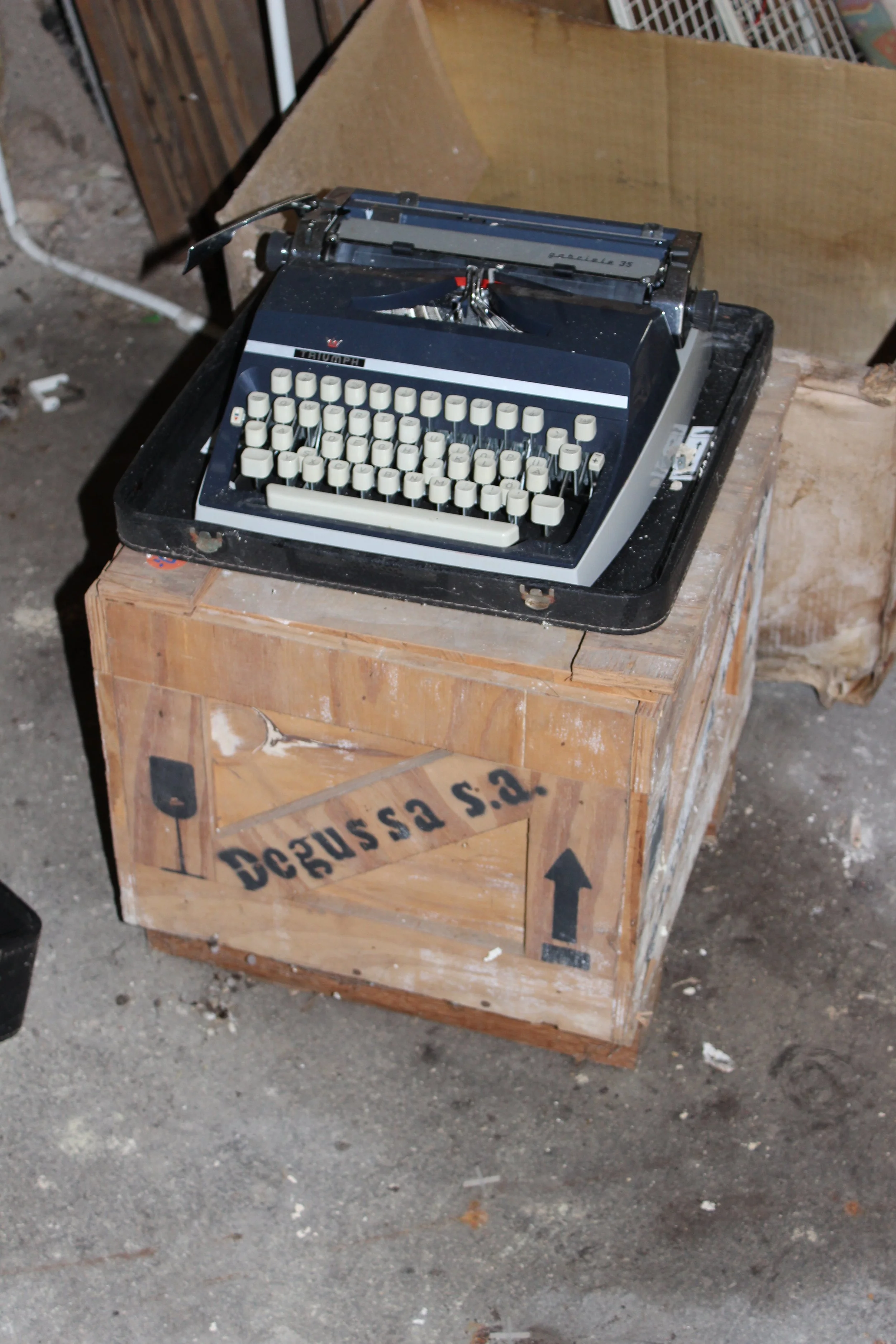 Alte Schreibmaschine auf einem Holzstapel in einer Werkstatt oder Lagerraum.