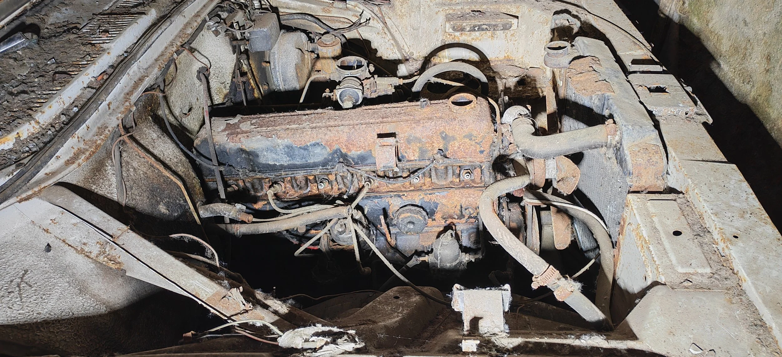 Ein alter, verrosteter Automotor, sichtbar in einem Motorraum, mit deutlichen Anzeichen von Korrosion und Ablagerungen.