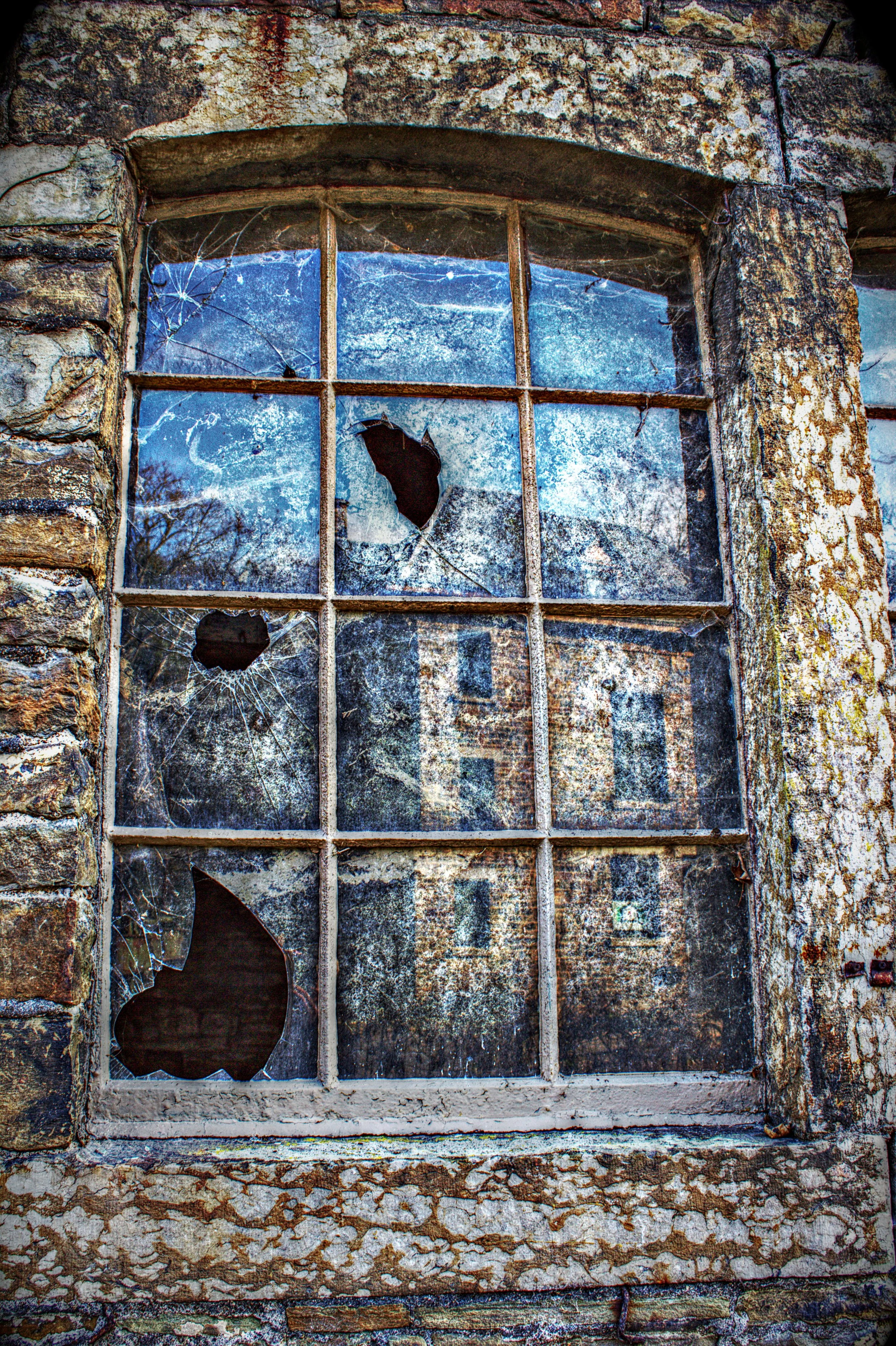 Ein verlassener Fensterrahmen mit zerbrochener Glasscheibe, umgeben von verwittertem Mauerwerk.