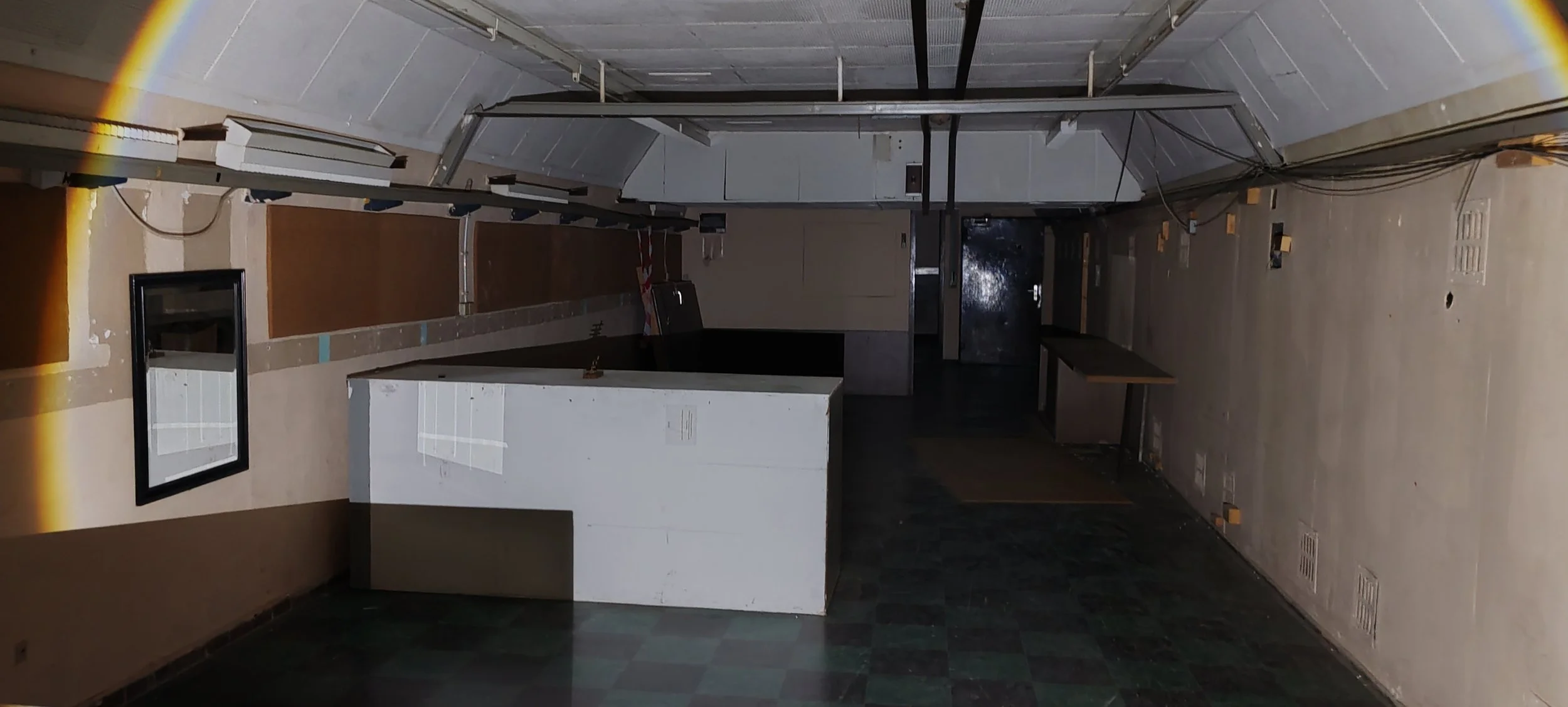 Ein leerer, dunkler Raum mit einer Theke im Vordergrund, Wänden und Böden, die renoviert werden, diverse Kabel und Rohre an der Decke.