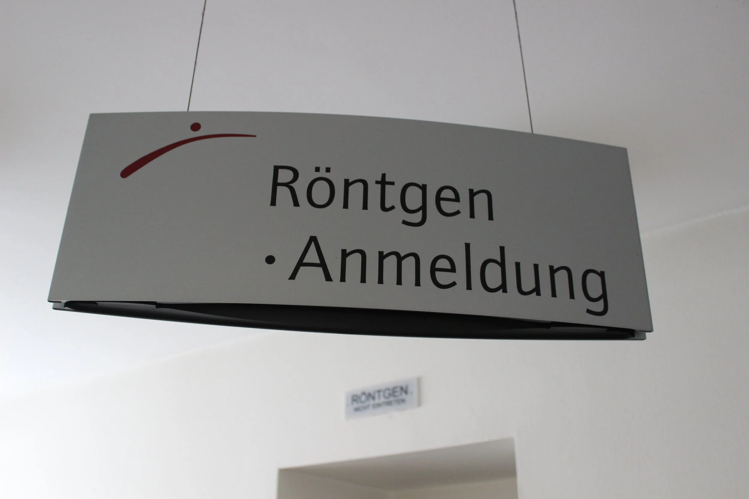 Hängendes Schild mit der Aufschrift "Röntgen. Anmeldung" in einem Wartebereich.